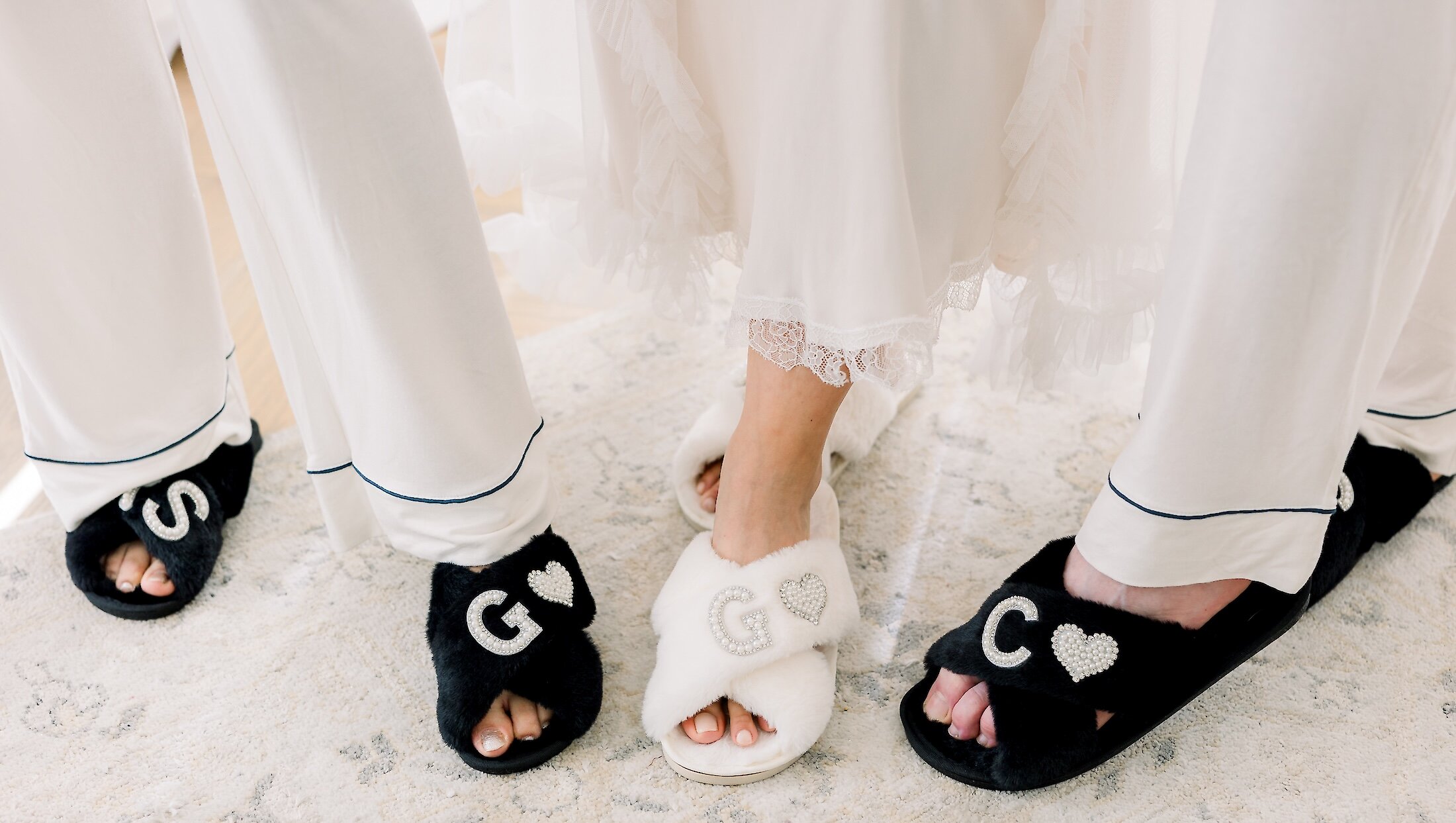 Close-up of the bridal party's feet wearing black and white fuzzy slippers personalized with white sequined initials for getting ready photos.