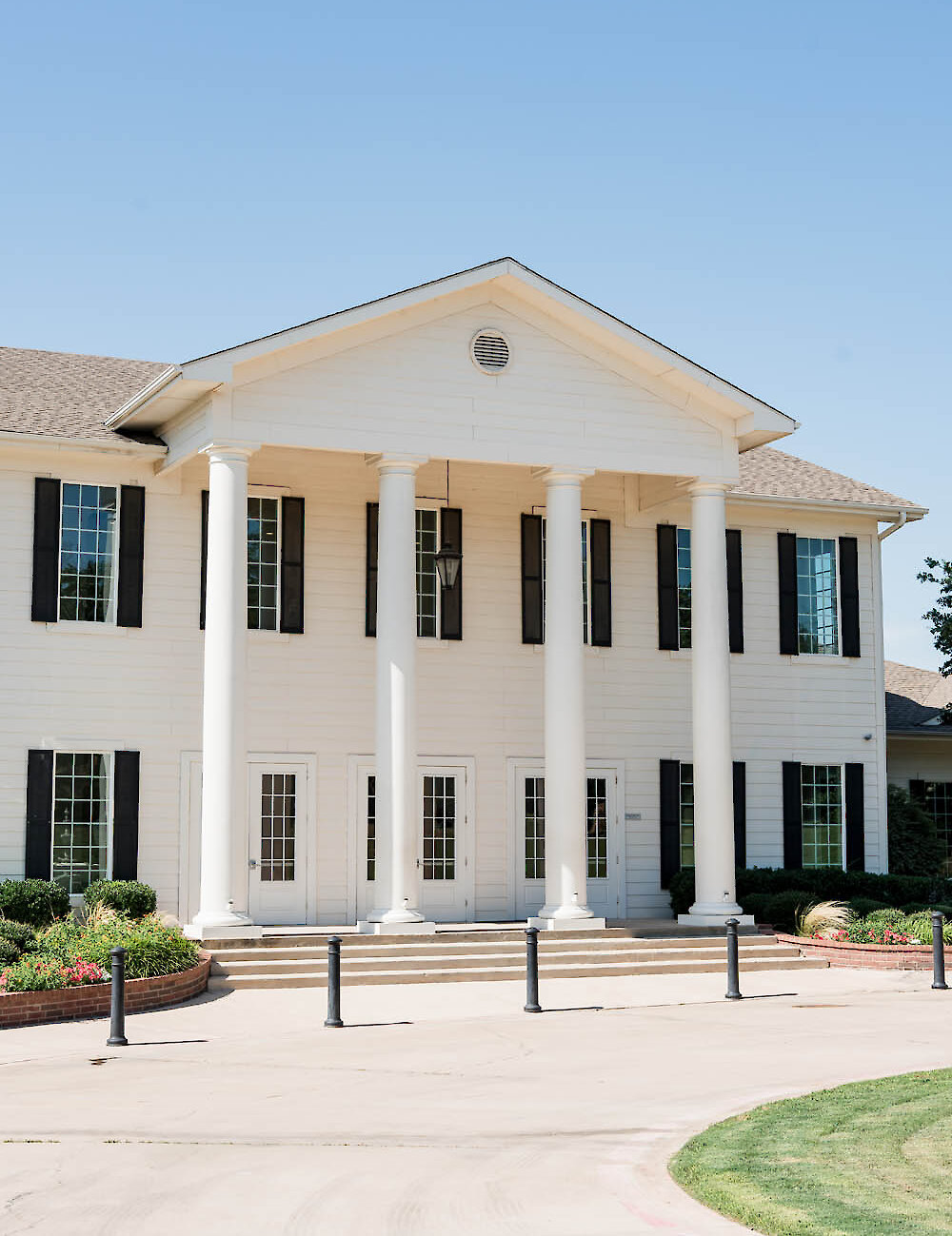 The exterior of a white Southern Colonial mansion wedding venue featuring a large portico with tall white columns and black shutters on a sunny day.