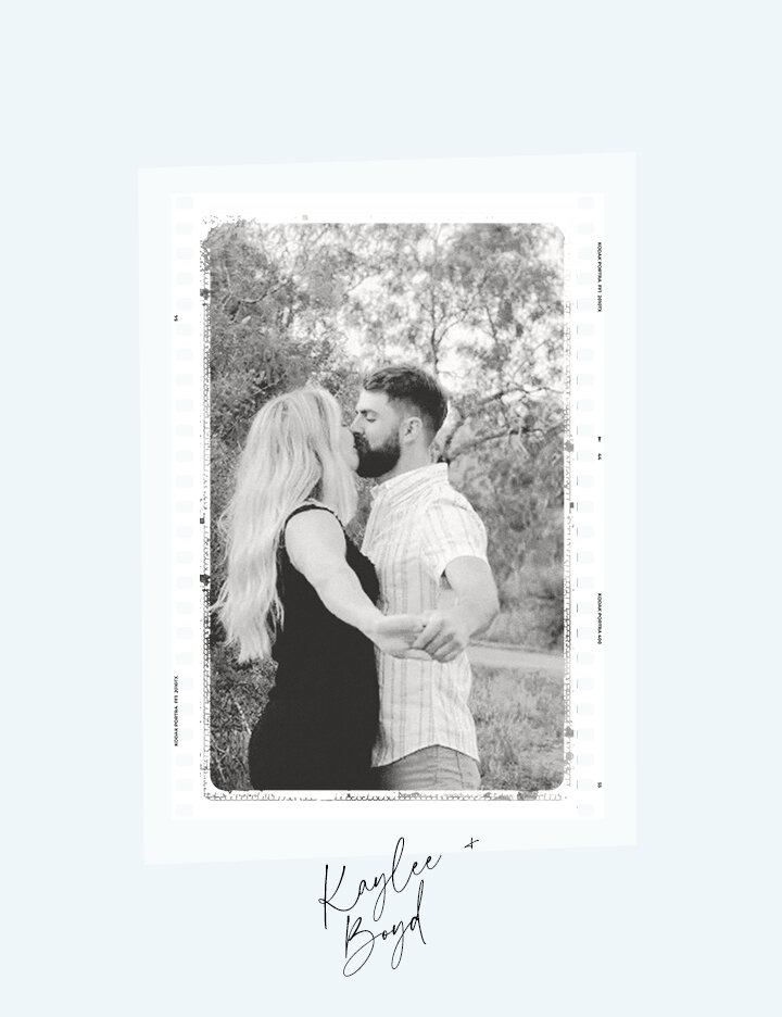 A black and white engagement photo of Kaylee and Boyd kissing outdoors, framed in a stylized strip border, holding hands while standing in a wooded area.