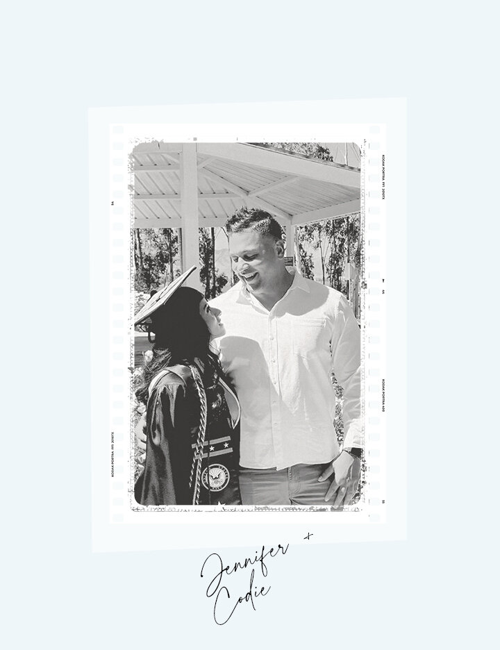 A black and white photo booth style portrait of Jennifer and Codie, with Jennifer wearing a graduation cap and gown, looking up at him.