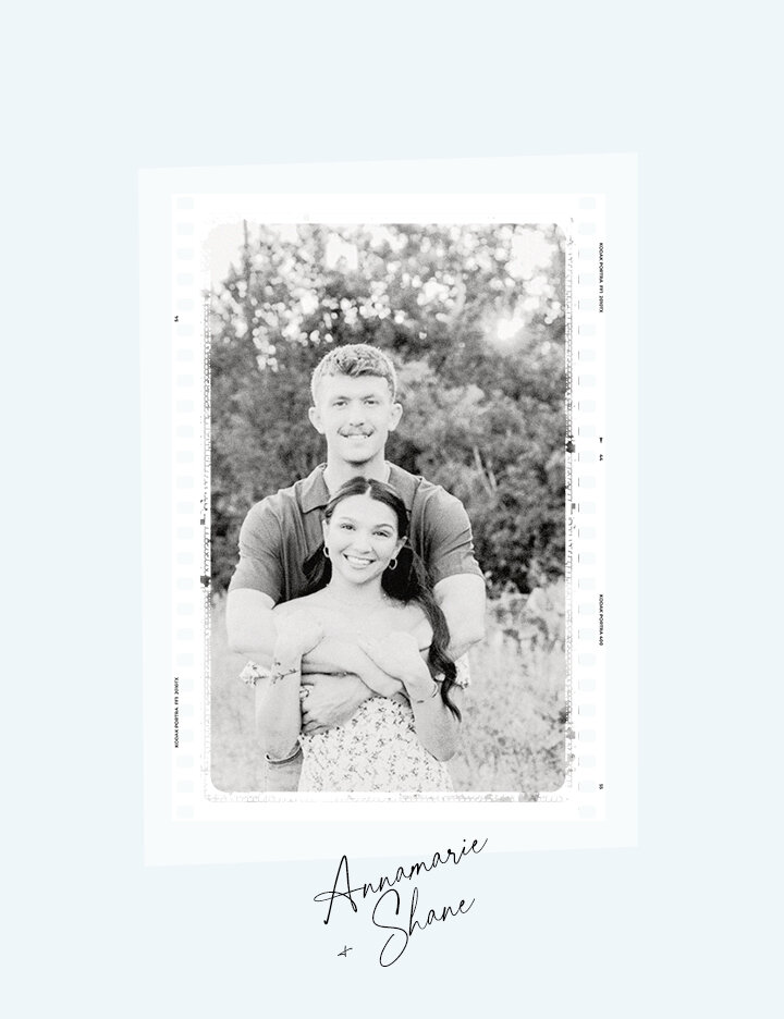 A black and white engagement photo of Annemarie and Shane embracing in a sunny field, with Shane standing behind Annemarie and holding her.
