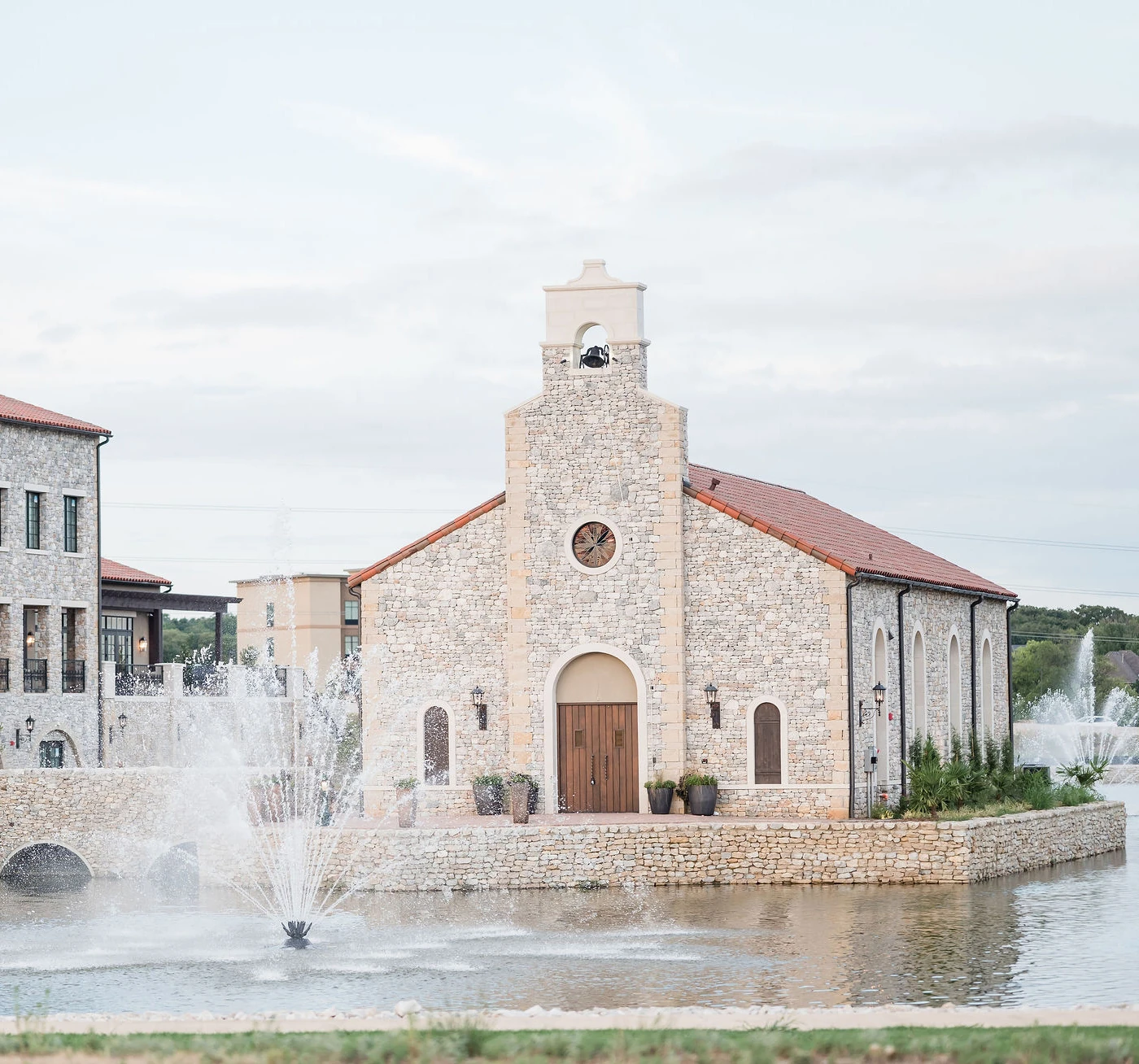 Scenic stone chapel wedding venue surrounded by water with large fountains and arched wooden doors