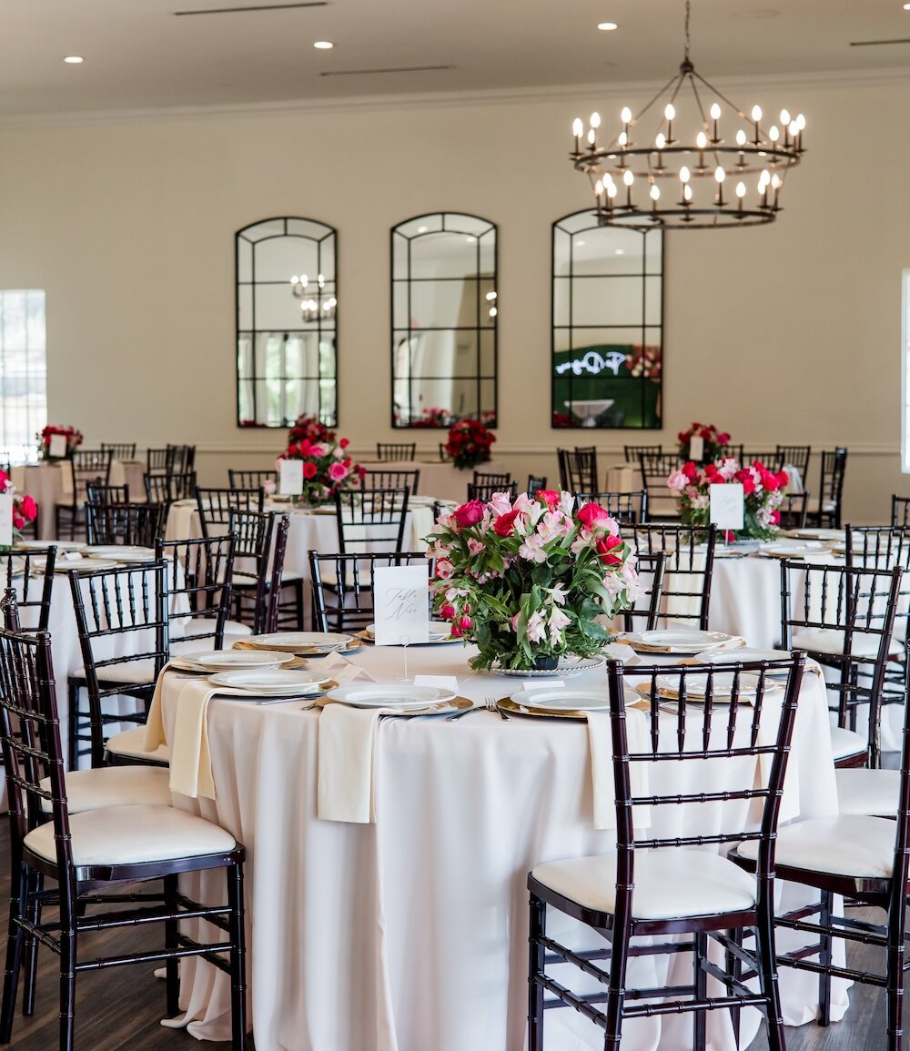 An elegant wedding reception ballroom set with round white linen tables, dark chiavari chairs, and three large arched mirrors on the back wall.
