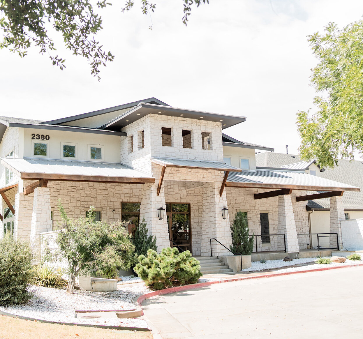 Exterior of a modern stone wedding venue with large windows, wood accents, and landscaped greenery at the front entrance