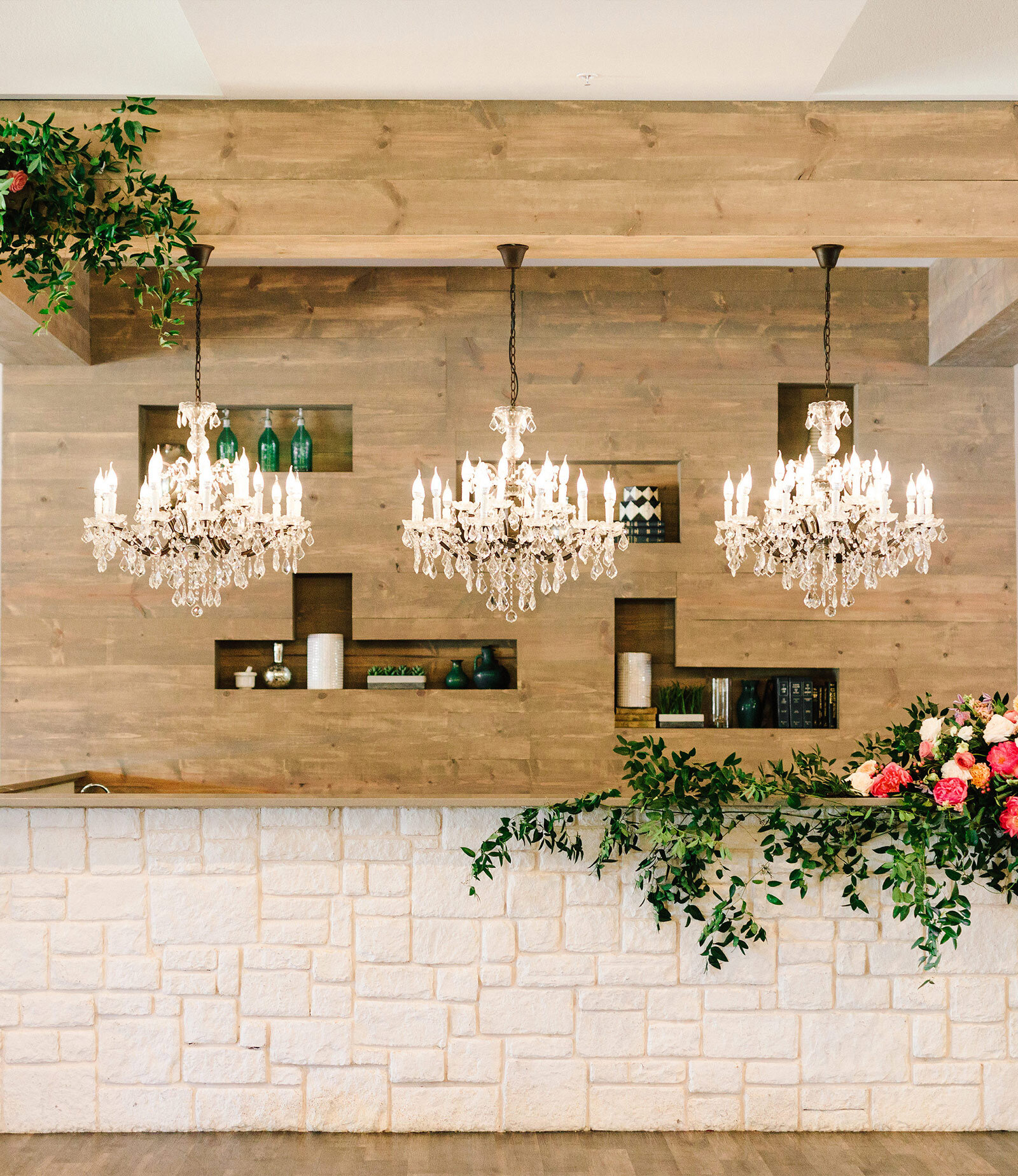 Elegant wedding reception hall featuring round tables set with white linens, clear ghost chairs, and navy blue napkins. The room has decorative pressed tin ceiling panels, wooden beam accents, and chandeliers.