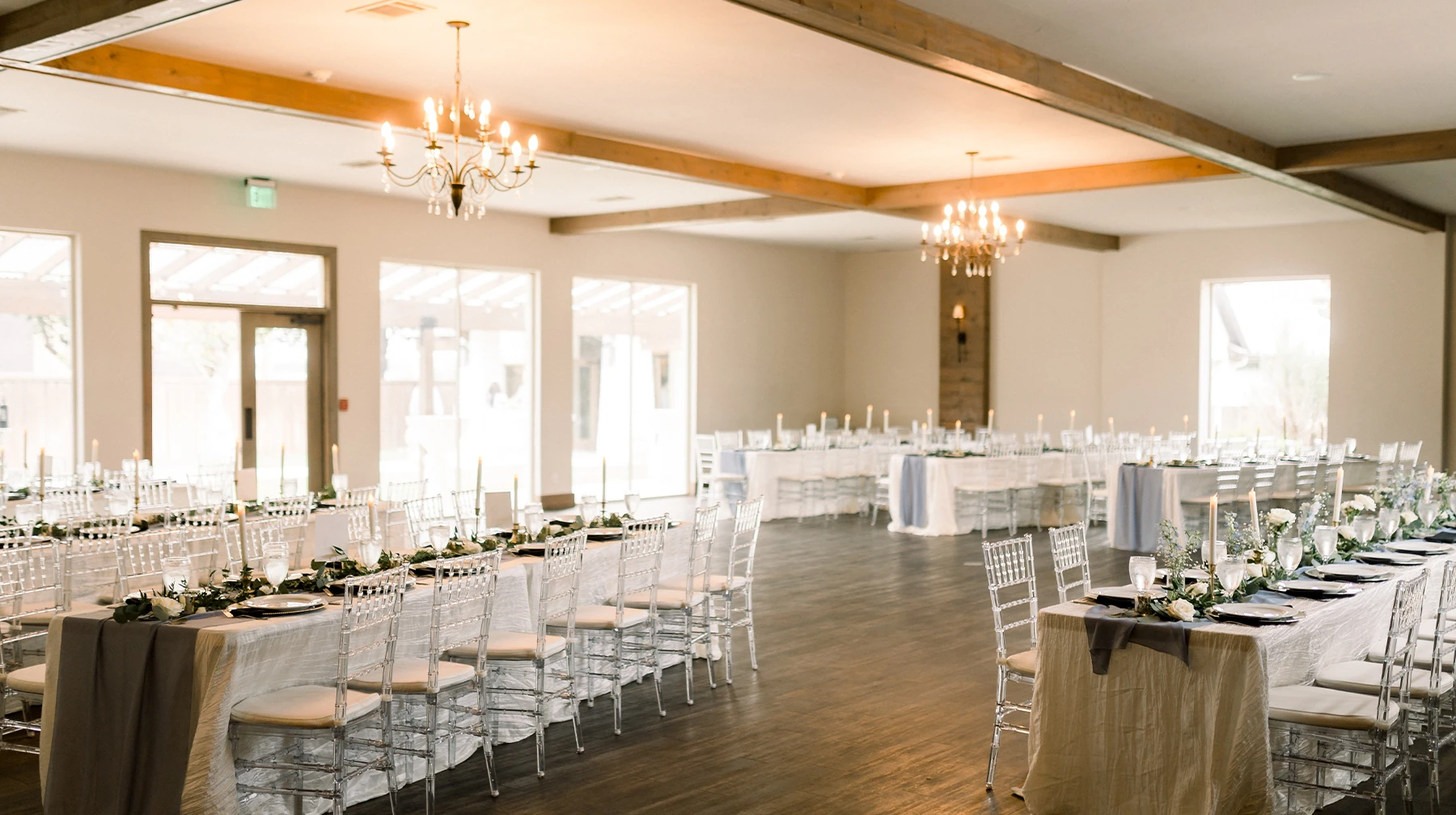 Indoor wedding ceremony setup with clear chairs facing a white stone fireplace decorated with candles, lanterns, and a floral arrangement