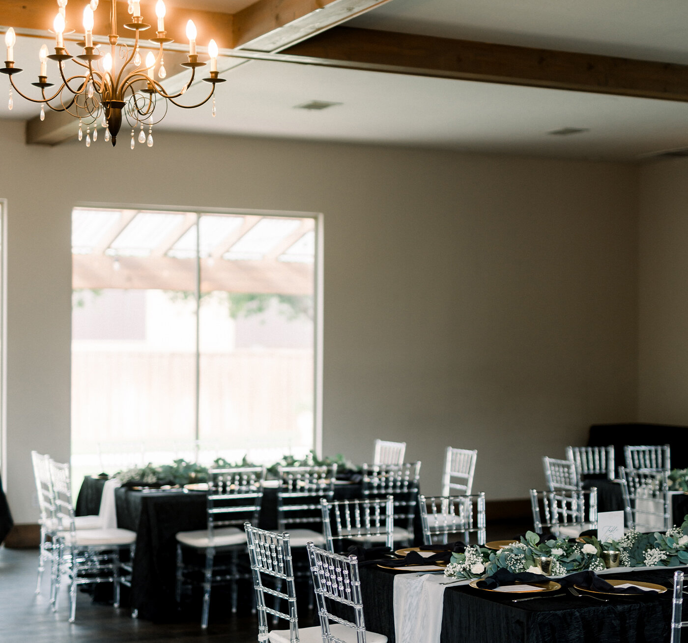 Elegant wedding sweetheart table with a simple white linen, set against a light stone wall. The front of the table is dramatically decorated with a massive, lush floral arrangement of white roses, hydrangeas, and greenery.