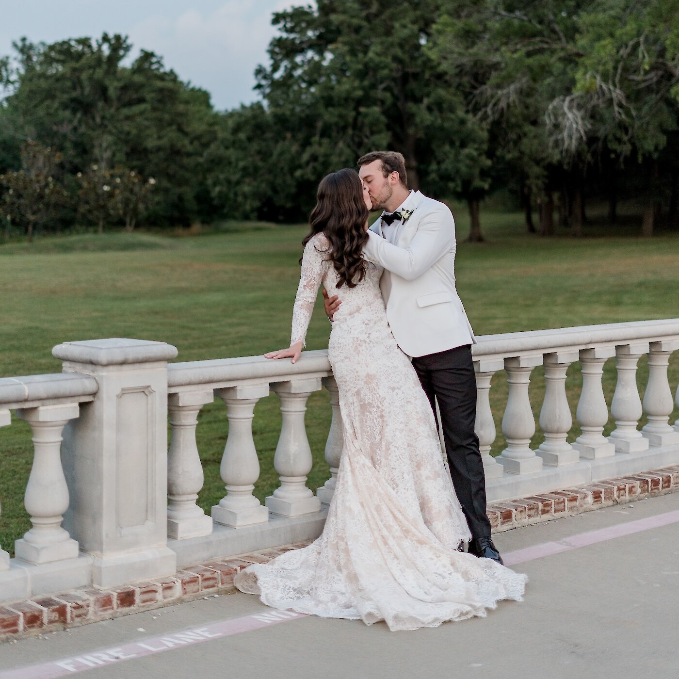Bride and groom sharing a kiss by a stone balustrade at dusk with the moon rising over a grassy landscape.