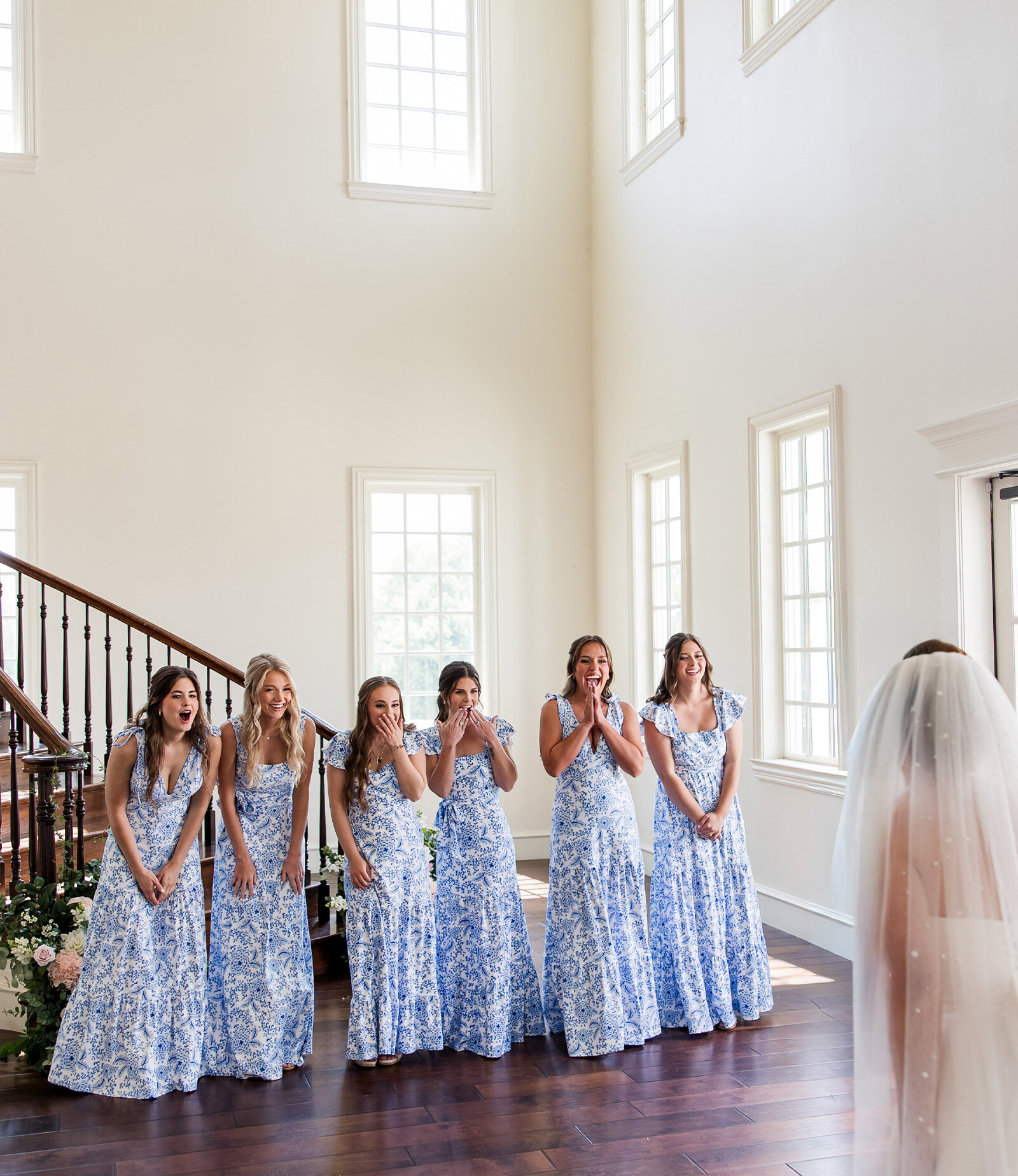 Elegant wedding reception hall with crystal chandeliers, long tables lined with white rose centerpieces, navy accents, and a tiered white cake near the bar.