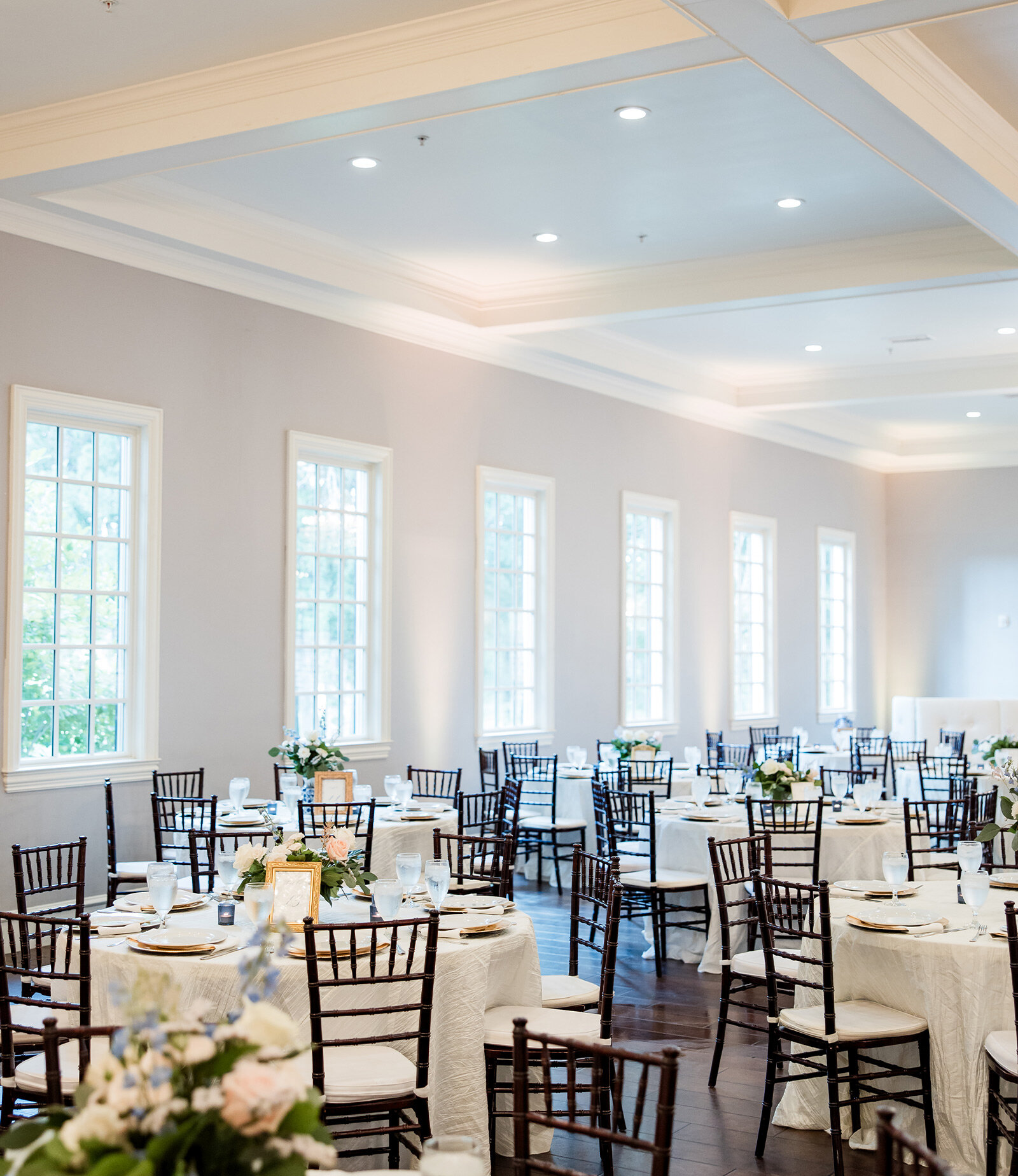 Elegant white Southern-style building with tall columns, black shutters, and landscaped entryway on a sunny day