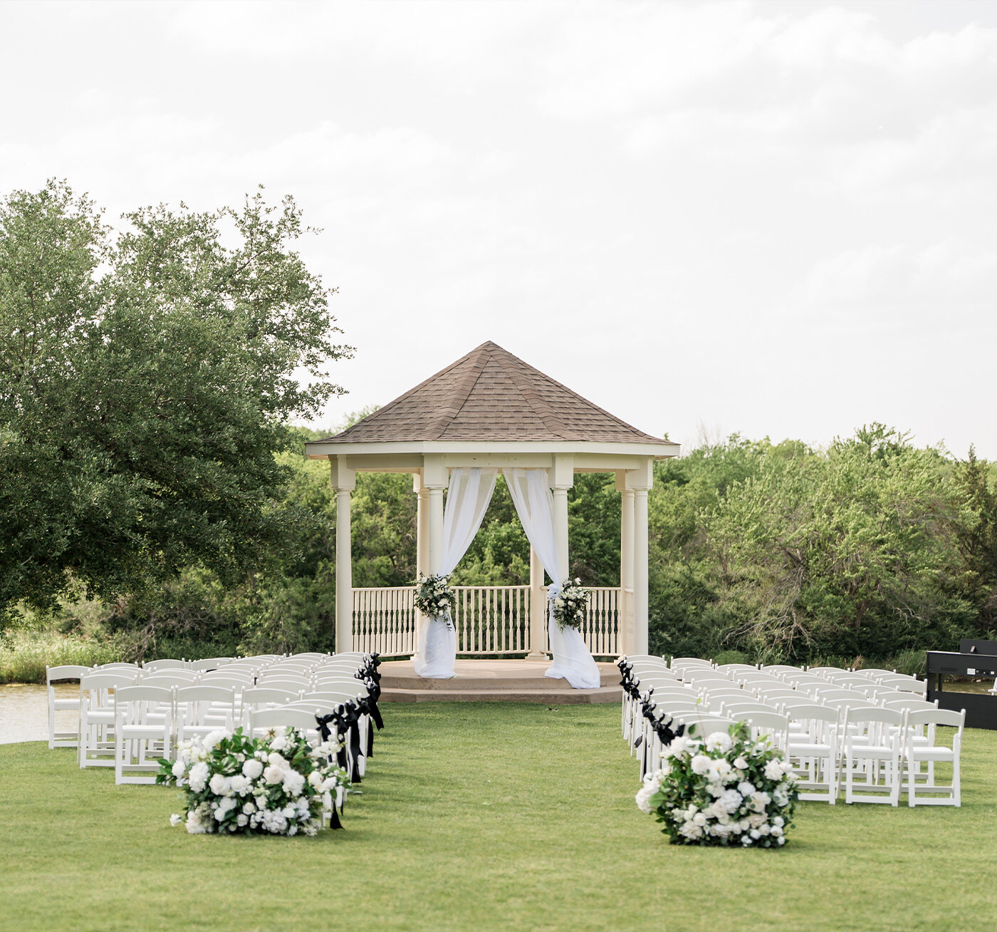Indoor wedding ceremony setup with clear acrylic chairs, dark wood floors, soft beige walls, elegant sconces, and a large grid-style window behind a minimalist podium.