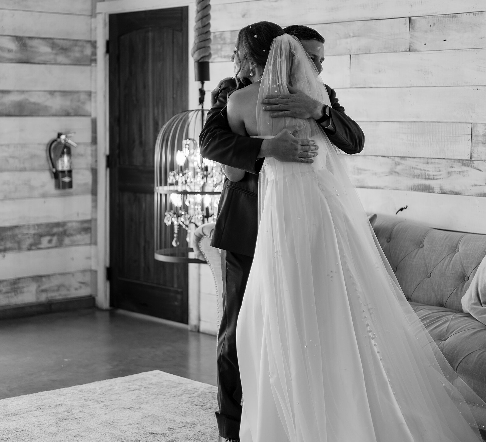 Bride shares an emotional hug with her father during their first look inside a rustic bridal suite
