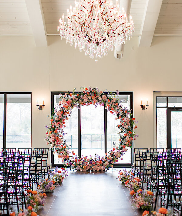 Modern ranch-style event venue with tall trees, stone column bases, large windows, and a covered entryway on a sunny day.