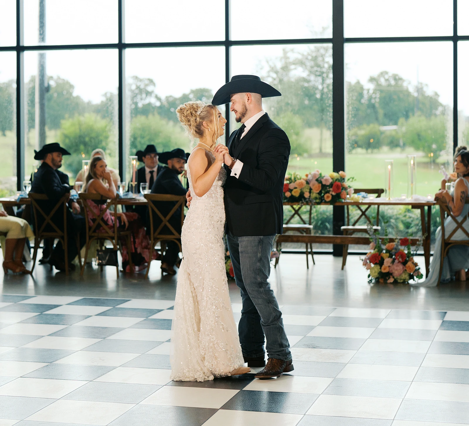 Bride and groom's first dance in a modern venue, featuring the groom wearing a black cowboy hat on a black and white checkerboard floor