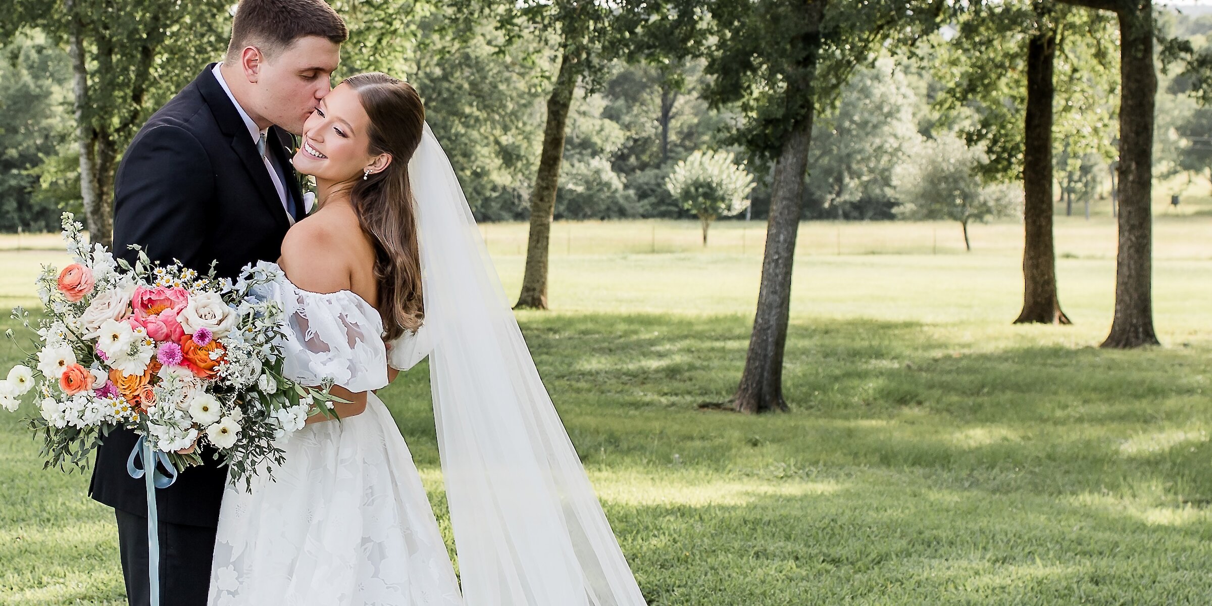 Groom kissing bride on temple while she holds her bouquet in a park-like setting