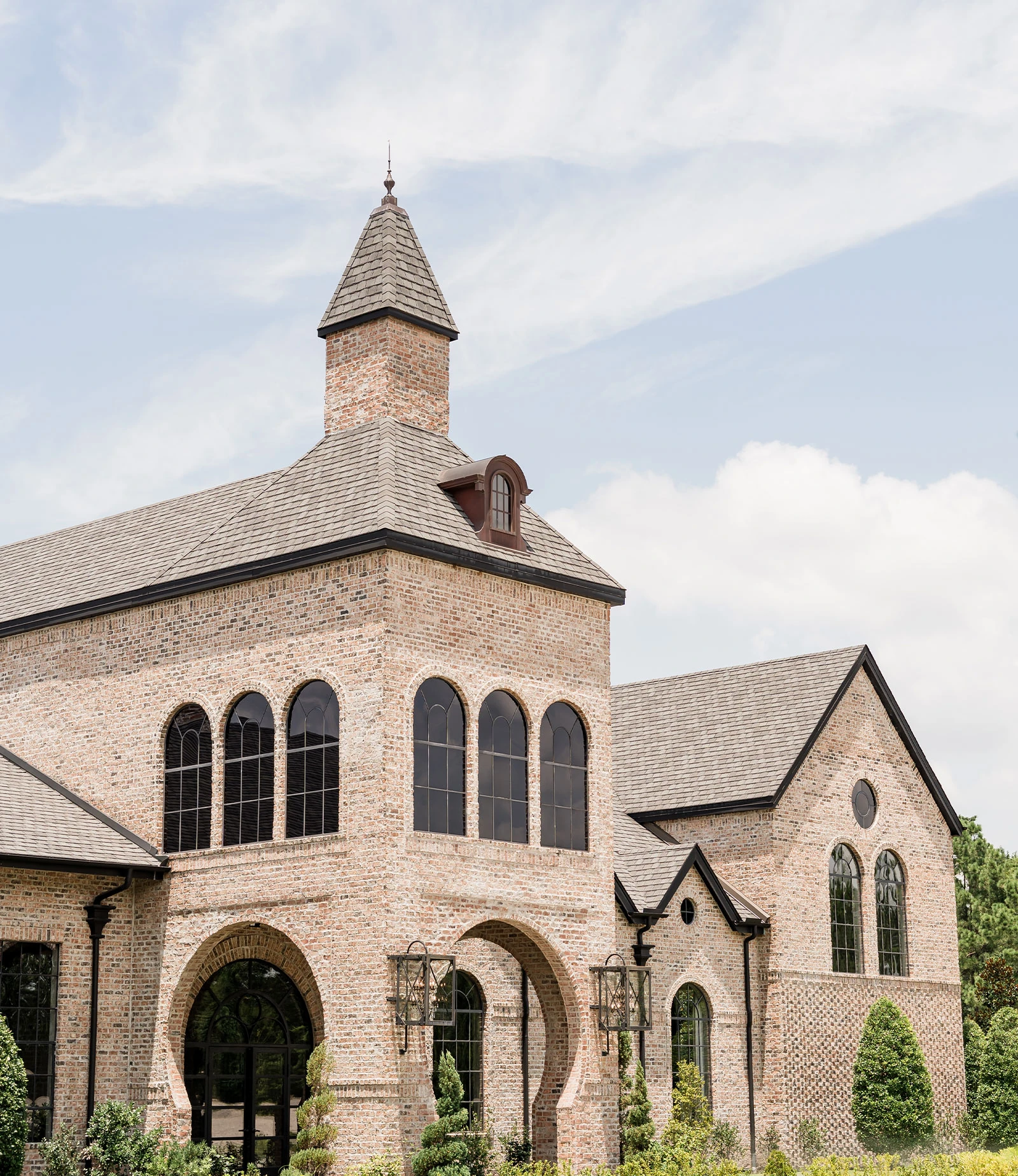 Modern wedding venue exterior featuring a long, covered entryway and stone-stacked columns set against a background of large oak trees