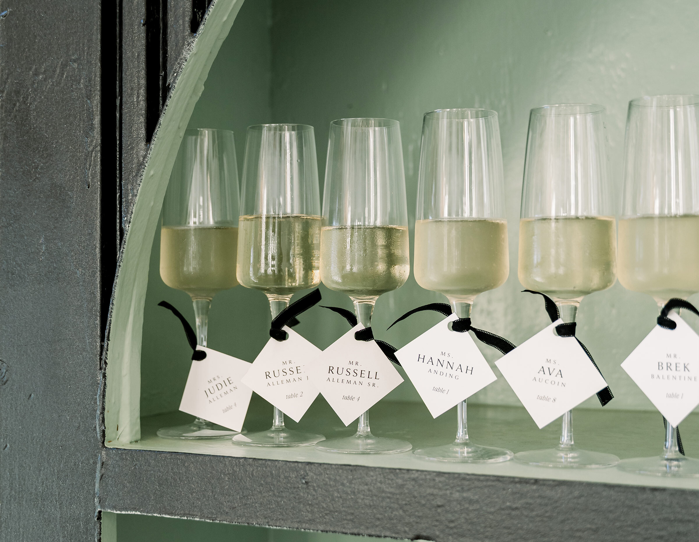 Five delicate champagne flutes filled with sparkling rosé wine are lined up on a serving tray in front of a window.