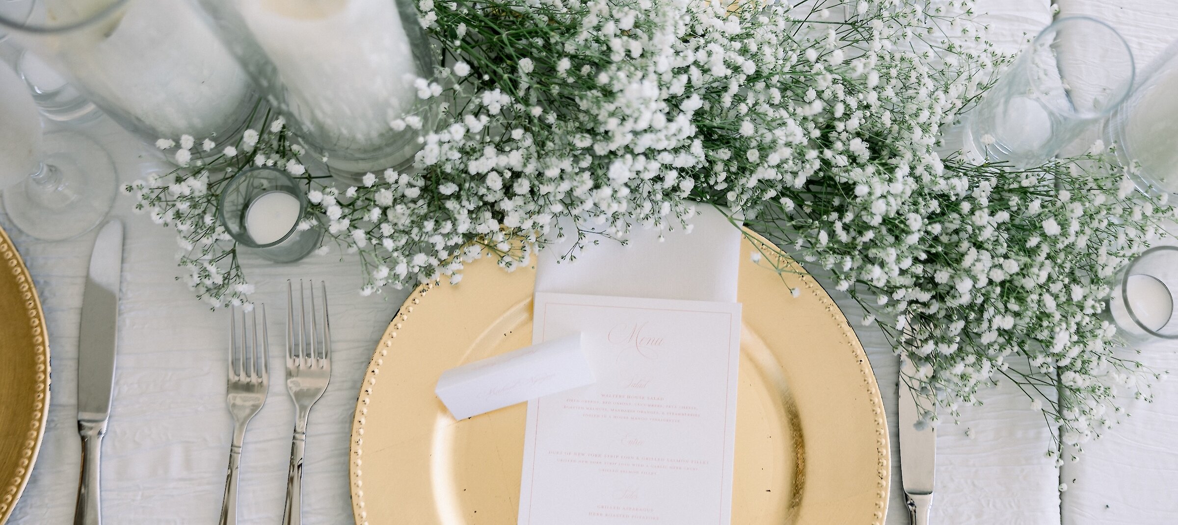 Wedding table place setting with babies breath flowers, white candles and gold plate