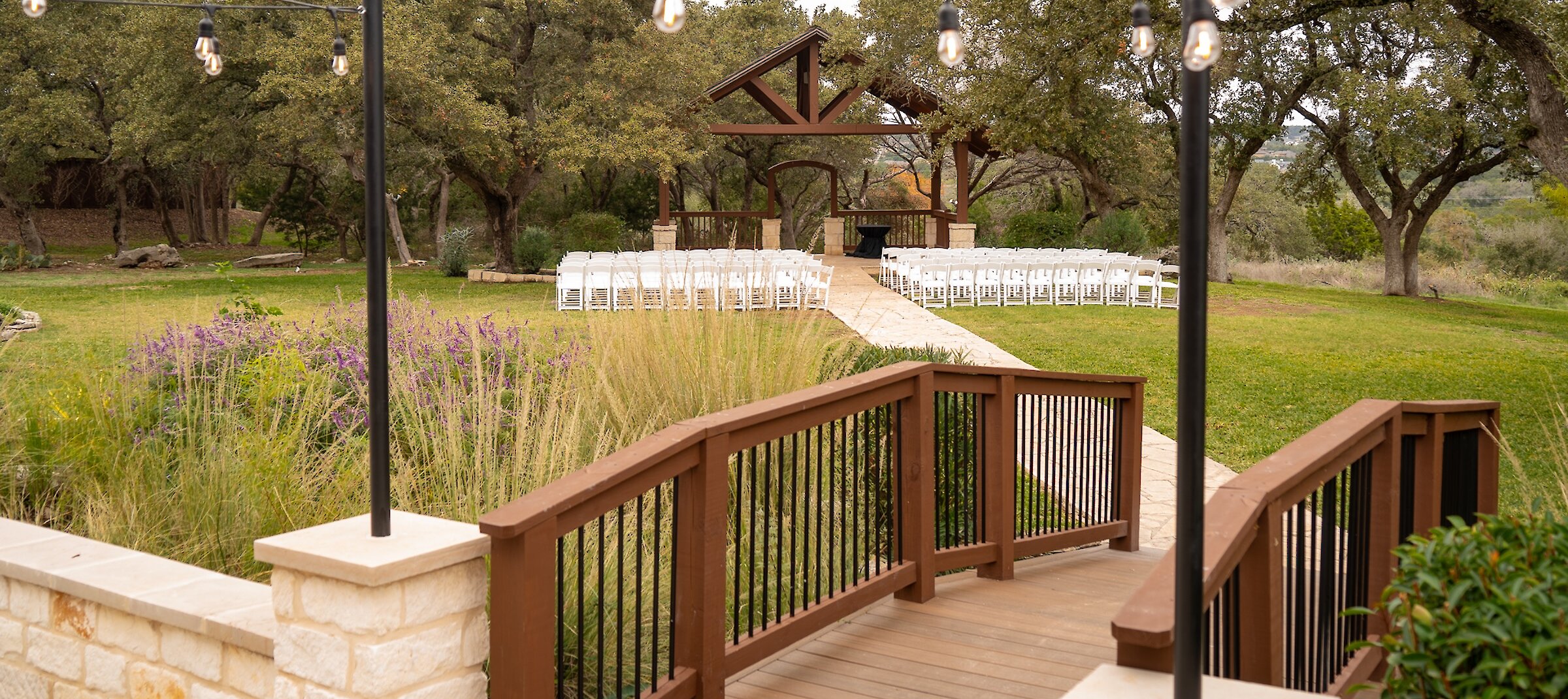 Wooden bridge leading to covered outdoor pavilion with arranged white seats at Stonehaven Hall wedding venue