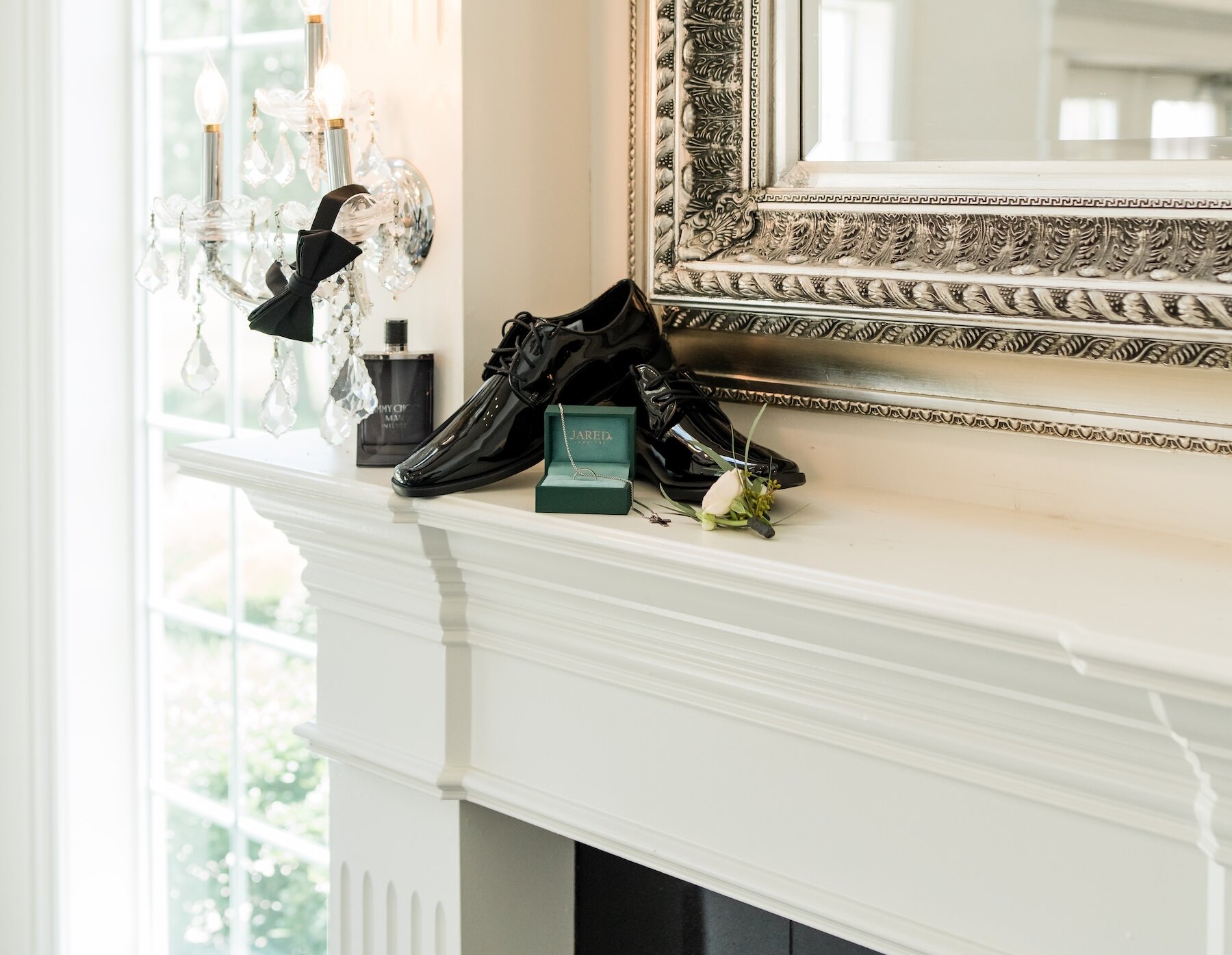 Groom's shoes, cologne and ring artfully arranged on fireplace mantle