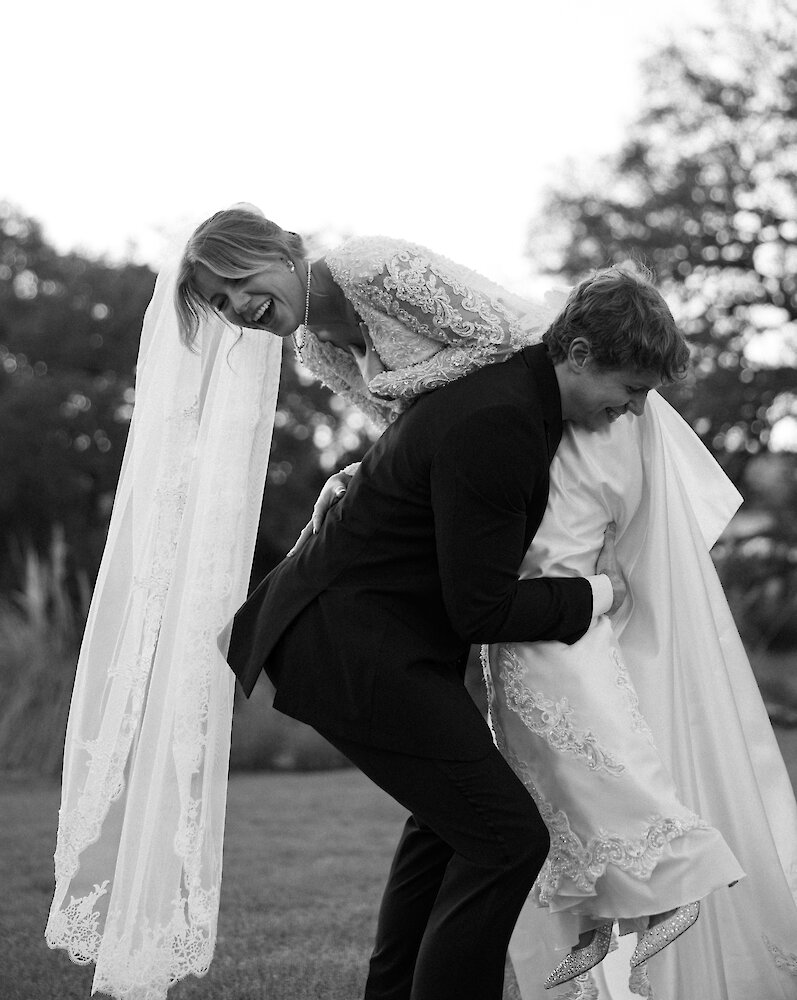 Black and white photo of groom lifting laughing bride onto his shoulder