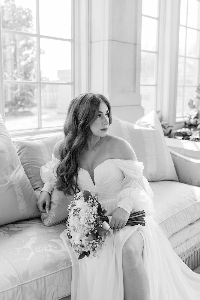 Black and white photo of a bride sitting on sofa holding her bouquet