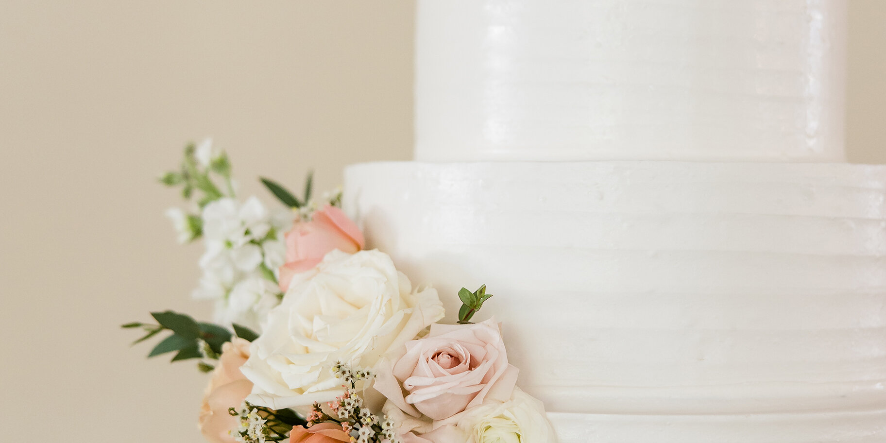 Three-tier white wedding cake decorated with blush and white roses, displayed on an ornate gold cake stand.