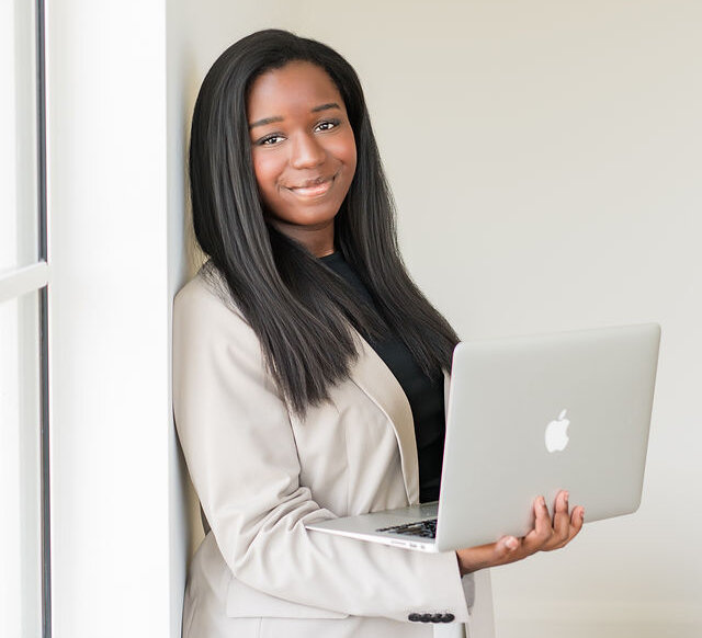 Professionally dressed woman looking at camera holding laptop