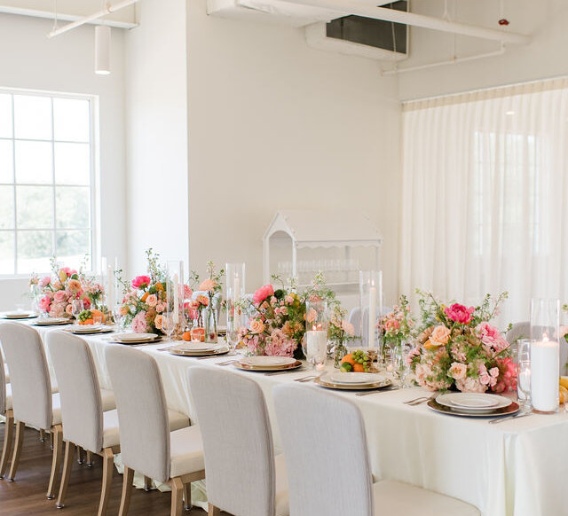 Set table with white tablecloth, plates, linens, candles and multiple bright floral displays