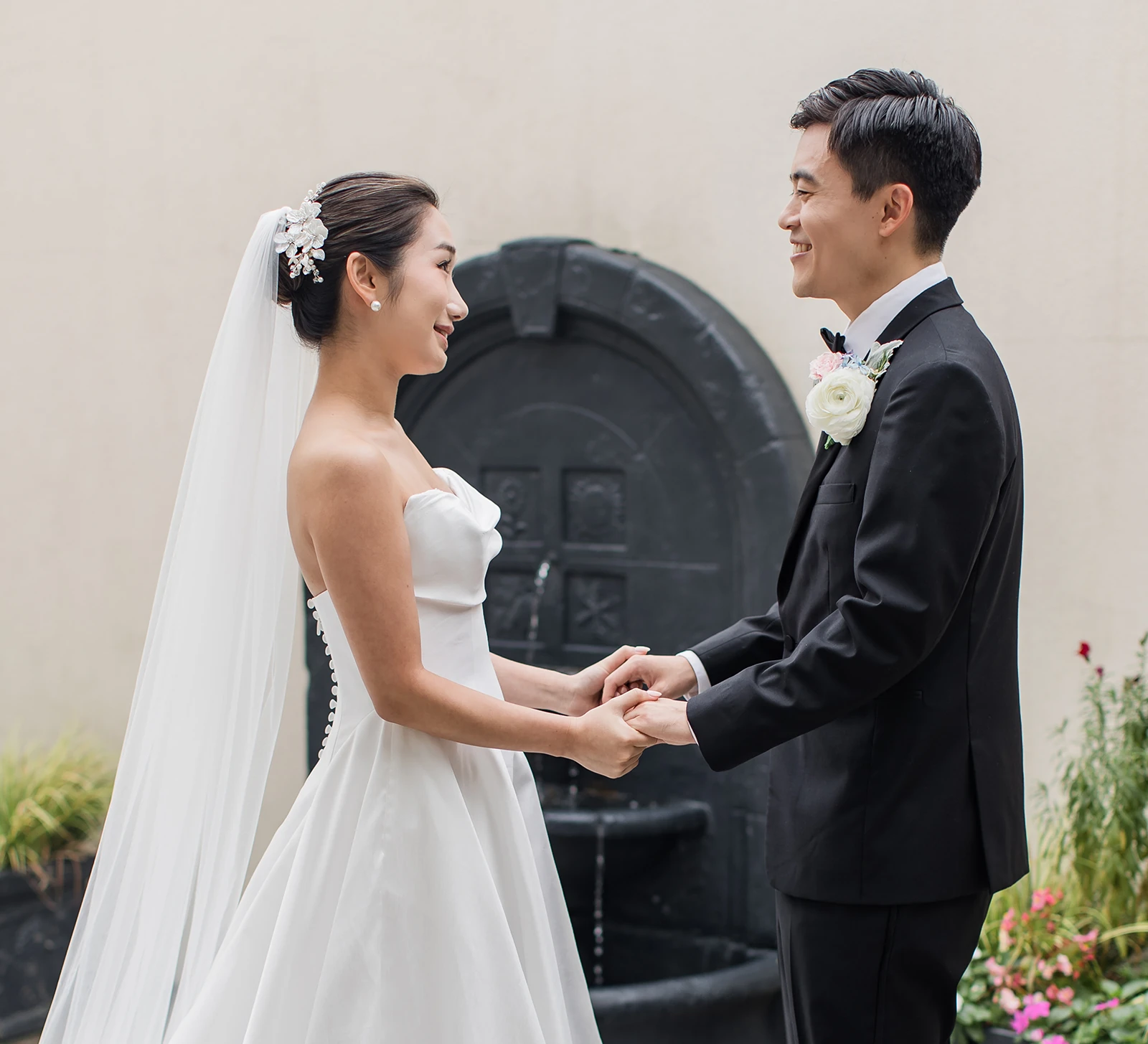 Bride and groom holding hands during first look in front of a black stone fountain