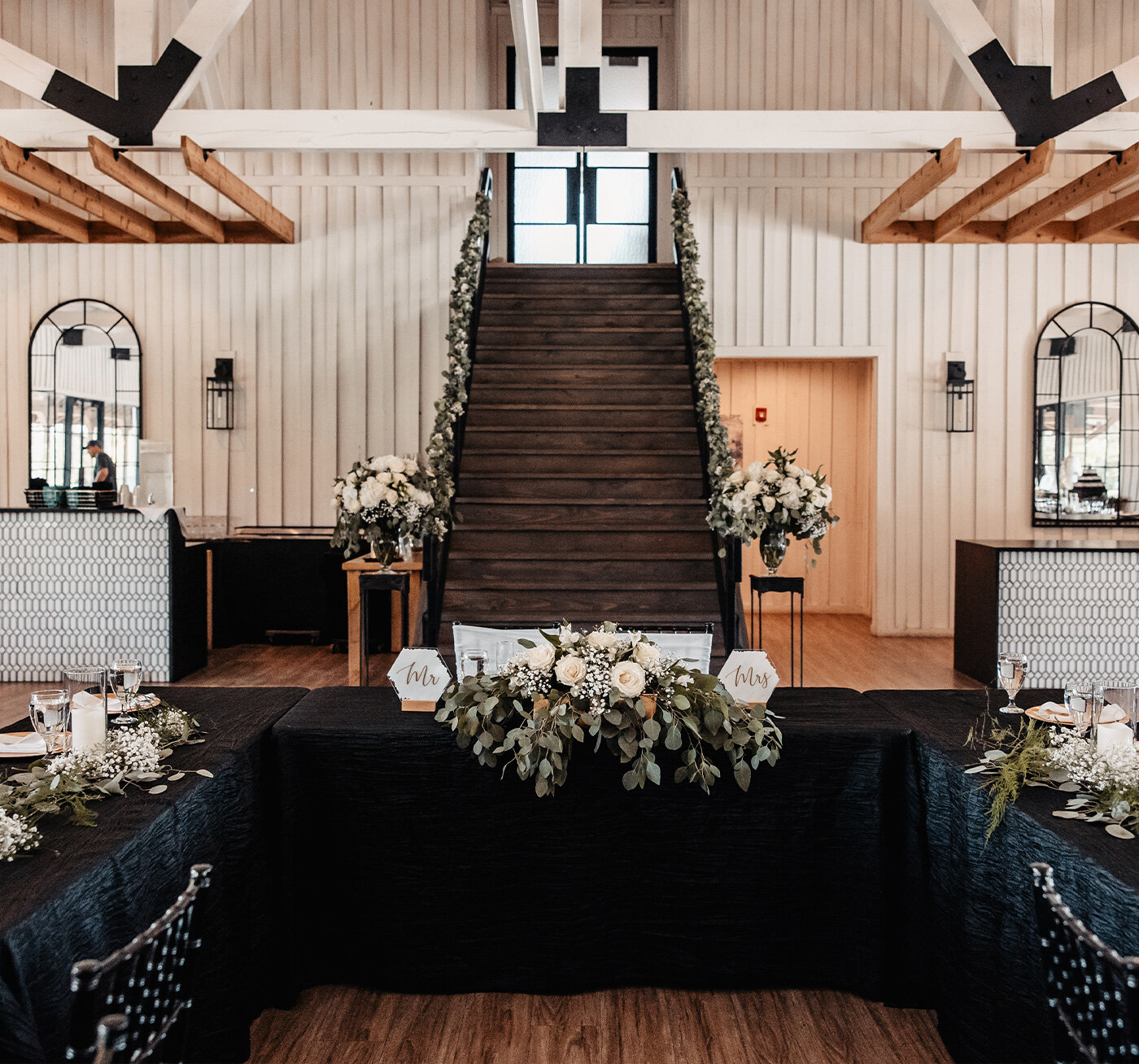 Group of groomsmen in black tuxedos raising beer bottles for a celebratory toast in the modern, well-lit groom's suite on the wedding day.