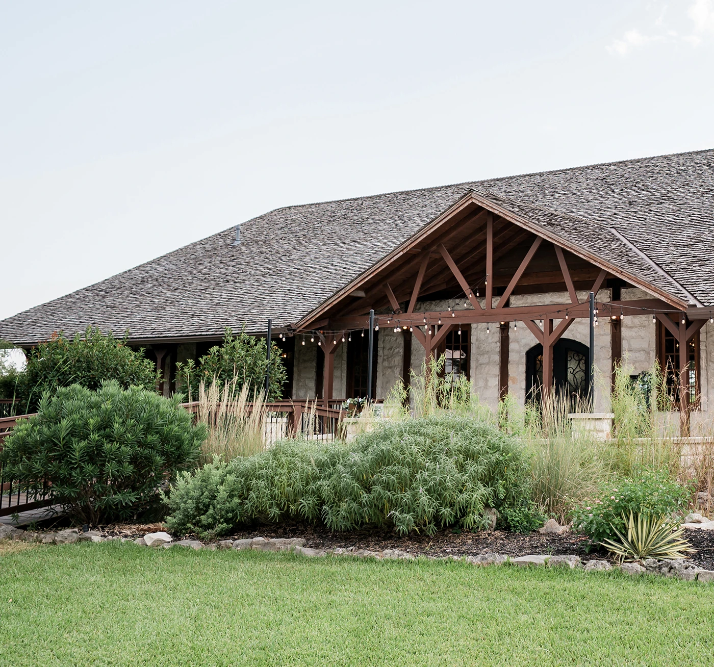 Rustic stone wedding venue with wooden beams, string lights, and lush garden landscaping