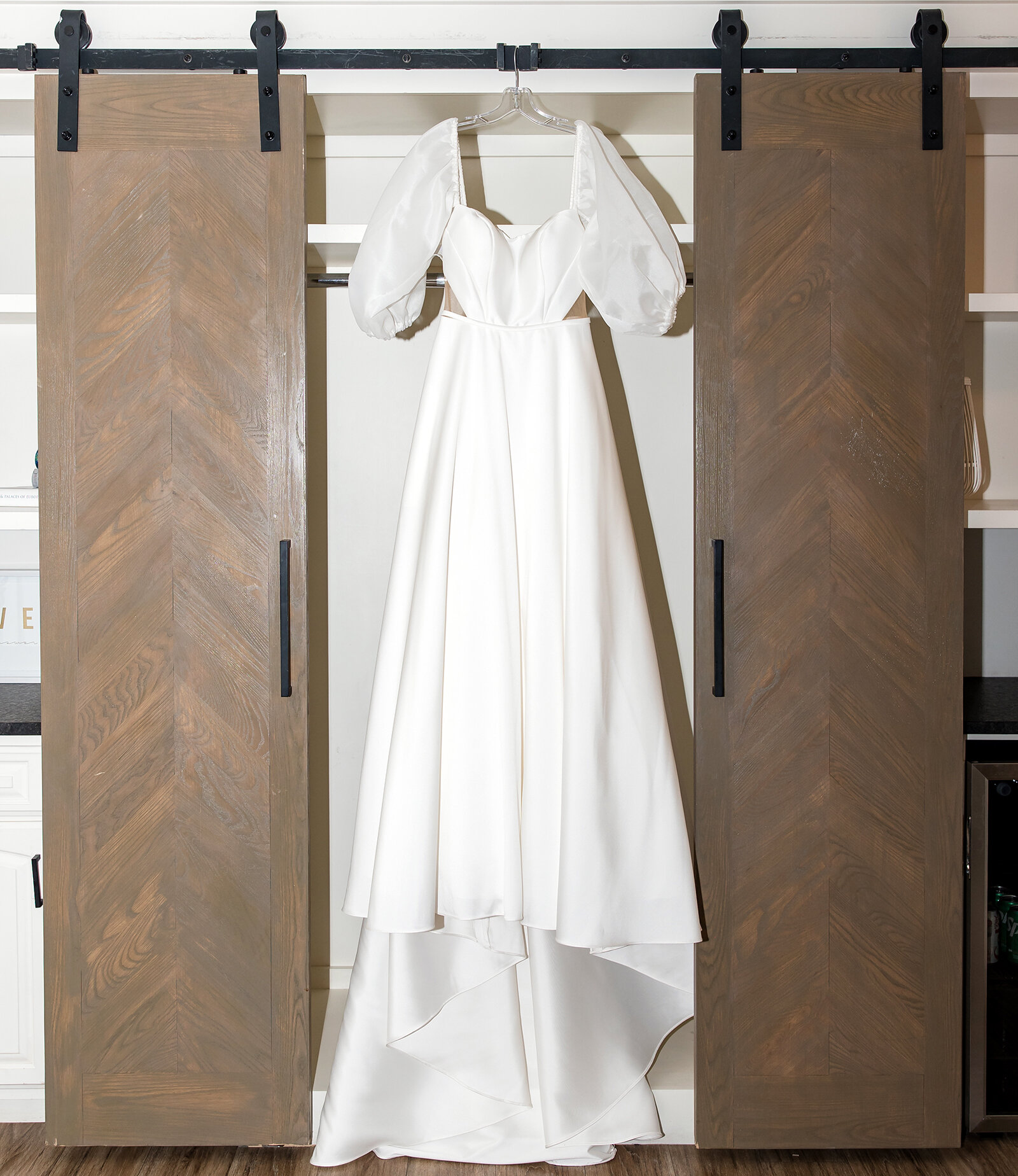 legant white wedding dress with puff sleeves hanging on a wooden barn door inside a bridal suite