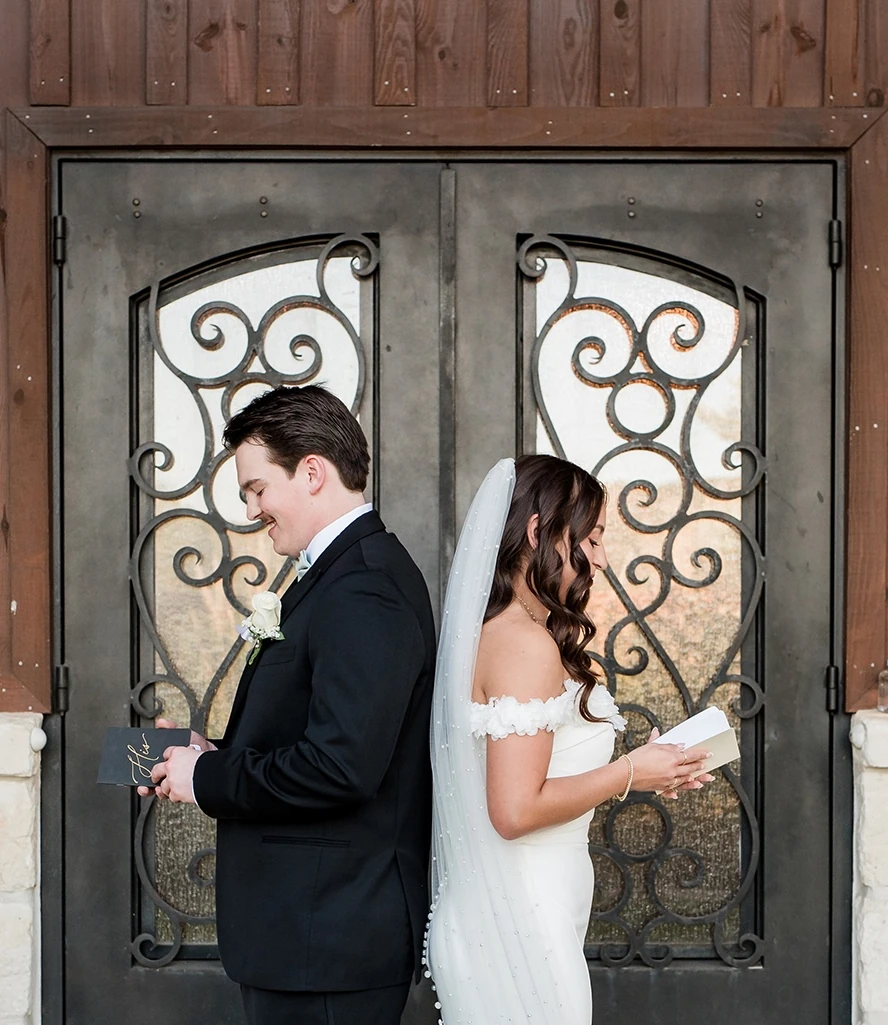 The bride and groom stand back-to-back, reading their personal vows outside black wrought iron doors before their wedding ceremony.