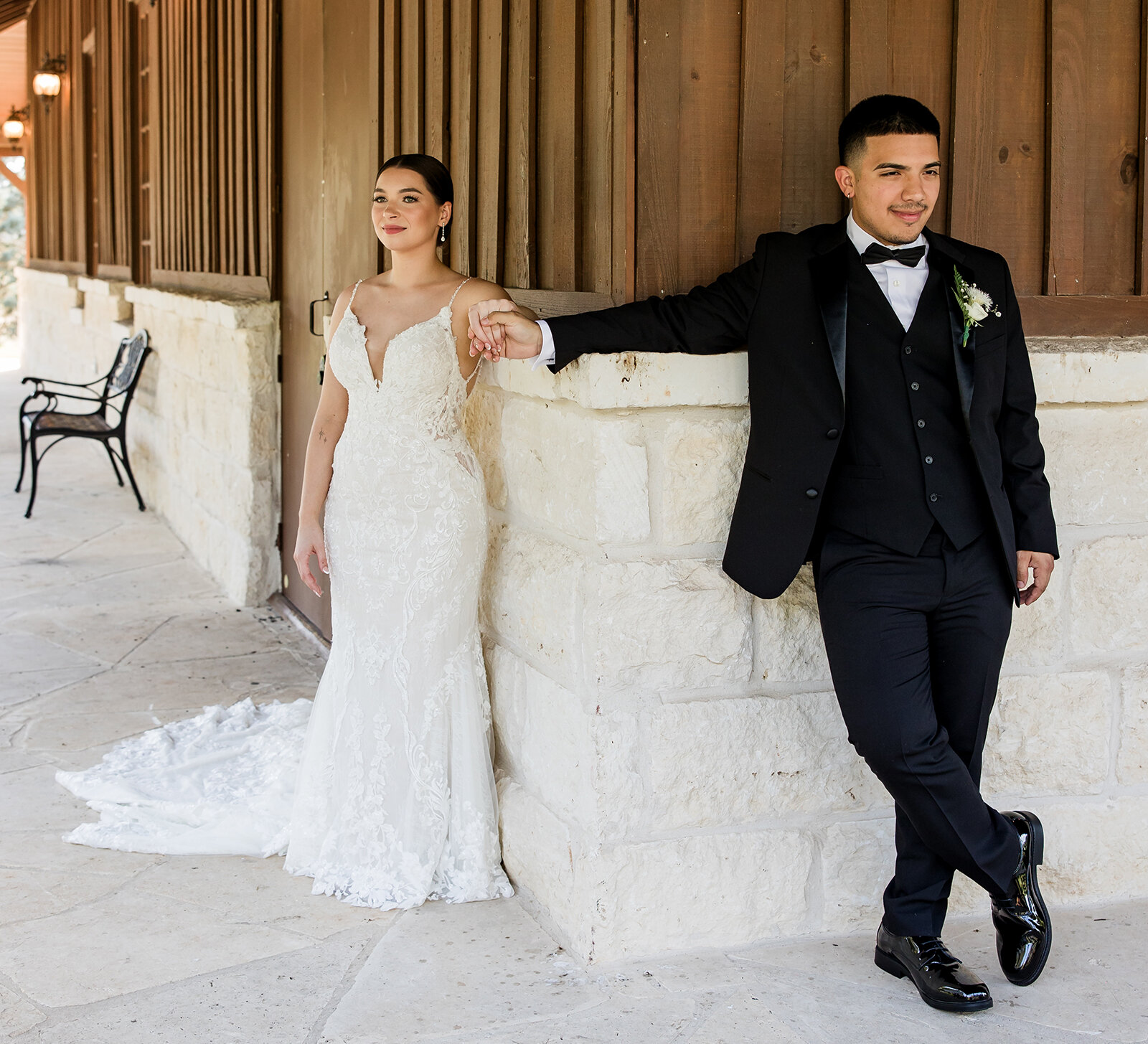 Bride and groom sharing a first touch around a stone wall at a rustic wedding venue, holding hands before the ceremony