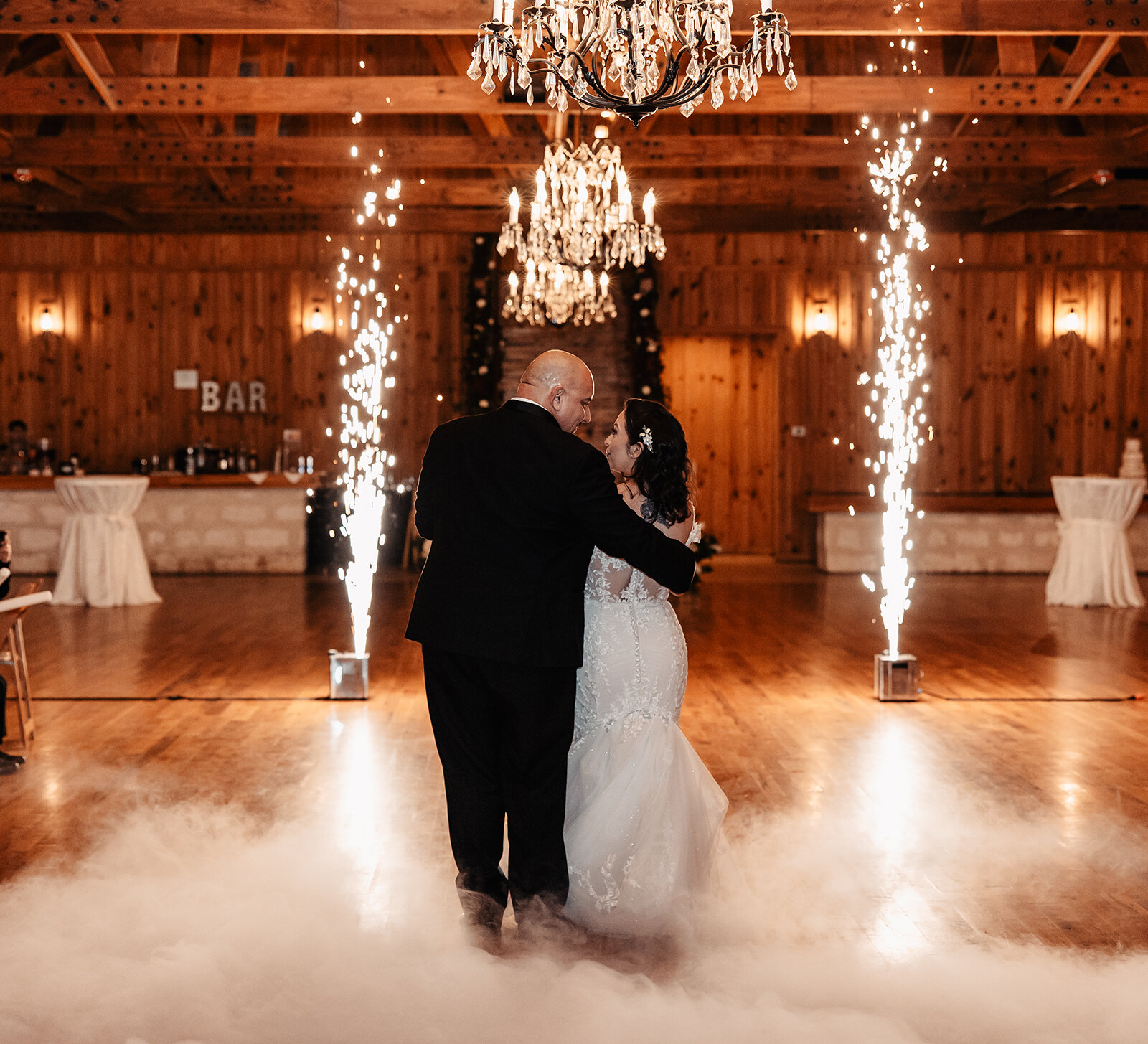Bride and groom sharing their first dance surrounded by indoor sparklers and low-lying fog at a warmly lit wedding reception