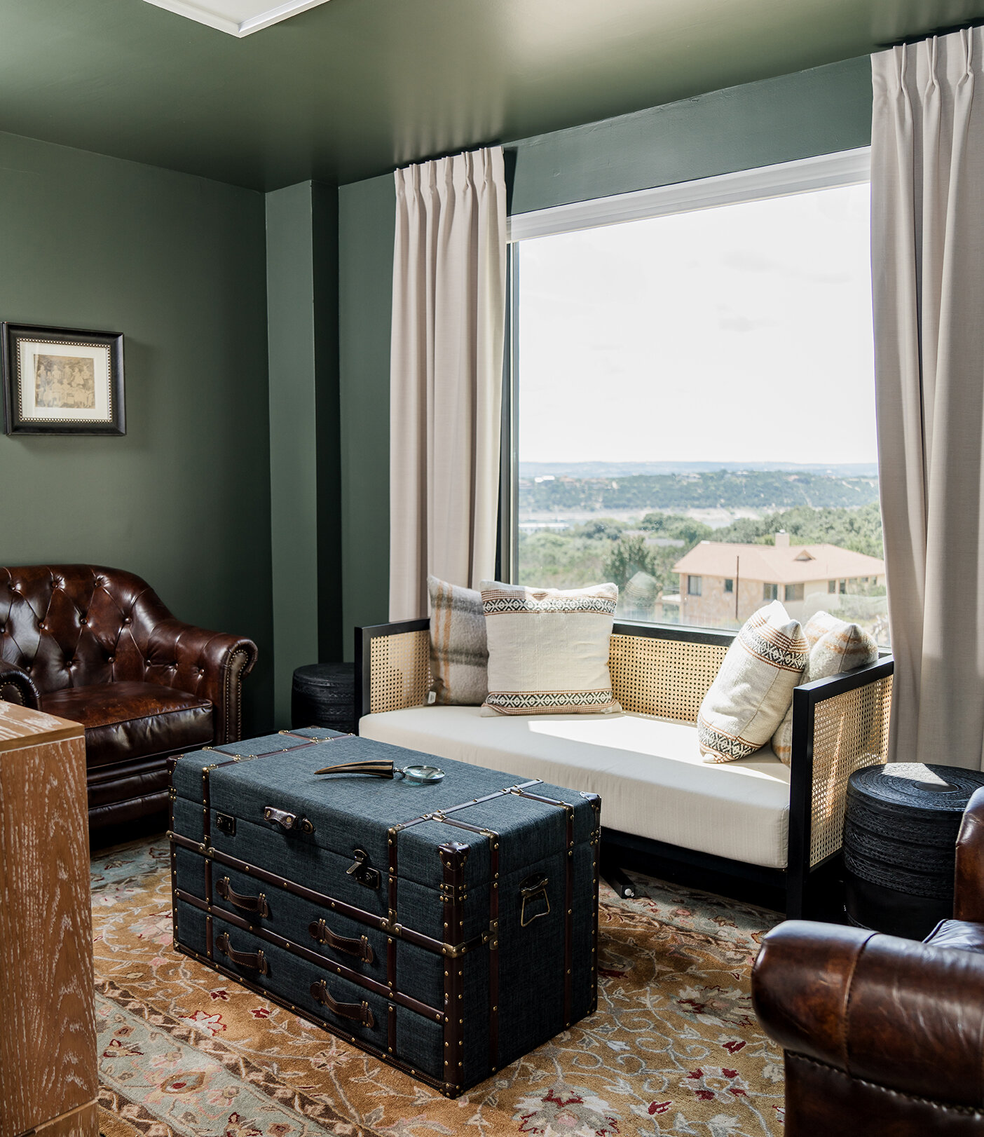 Cozy lounge room with leather sofas, a vintage trunk coffee table, a cushioned bench, and a large window overlooking scenic views