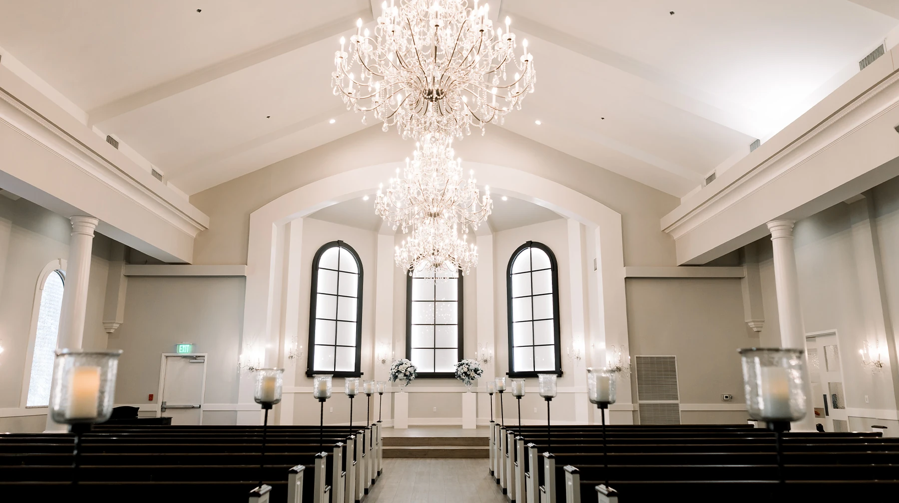 Joyful wedding recessional with the newlyweds walking through a tunnel of raised hands created by their wedding party. The bridal party is dressed in navy blue suits and light blue chiffon dresses outside a stone chapel with a bell tower.