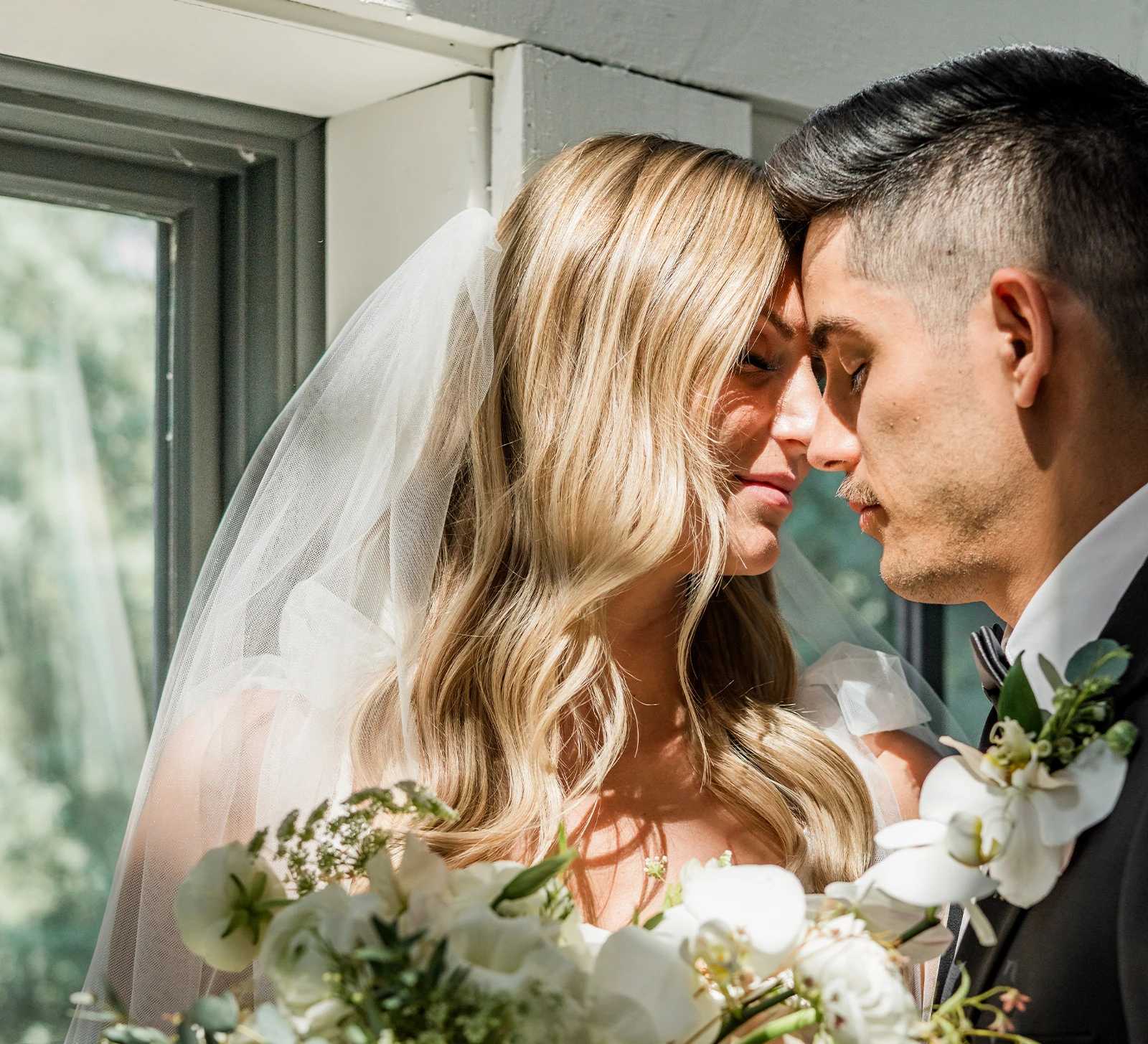 Bride and groom standing on grass, showing red and pink rose wedding bouquet