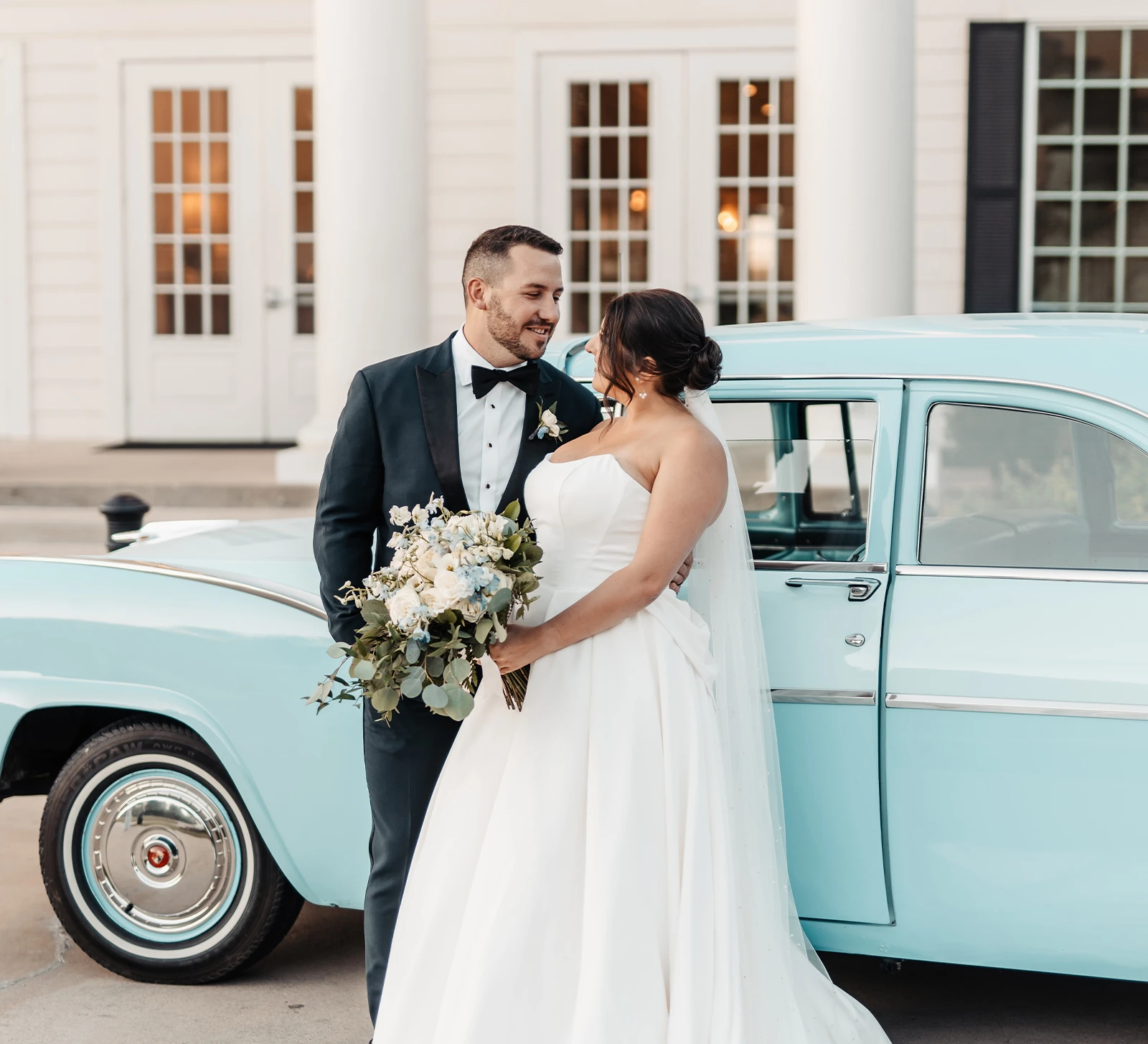 Bride and groom kissing, holding a classic white rose and baby's breath bouquet.