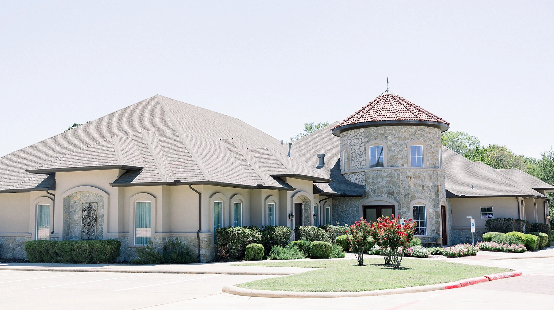 Exterior view of a wedding venue with stone architecture, a round tower, manicured landscaping, and bright daytime lighting