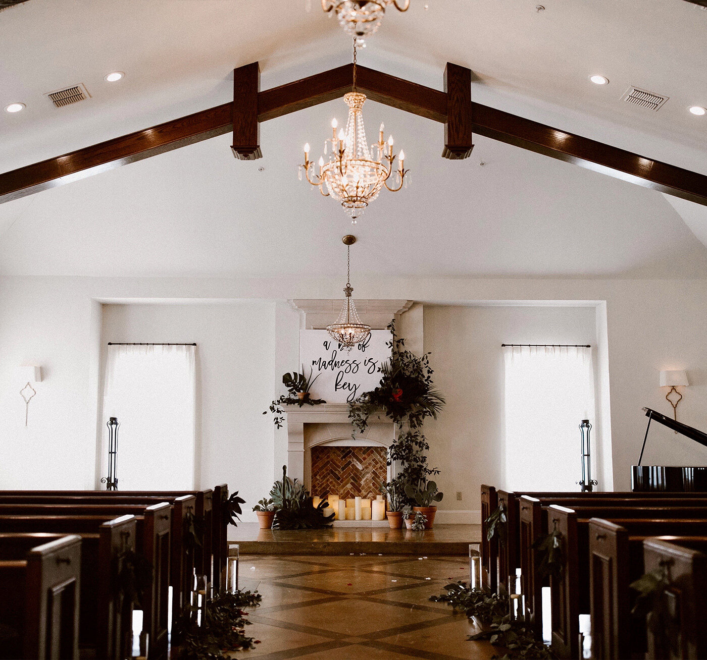 Exterior of a stone wedding venue featuring arched wooden doors, manicured shrubs, and a colorful landscaped garden
