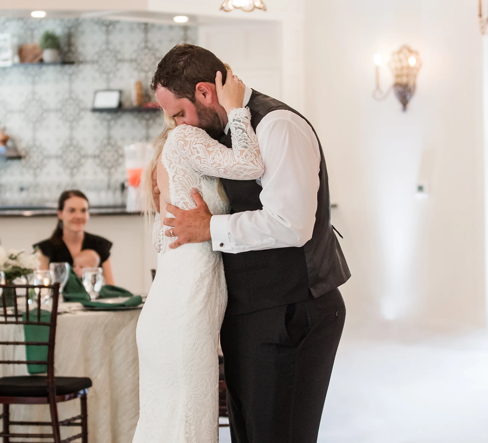 Bride and groom sharing an emotional hug during their first dance at the wedding reception, with guests watching in the background.”