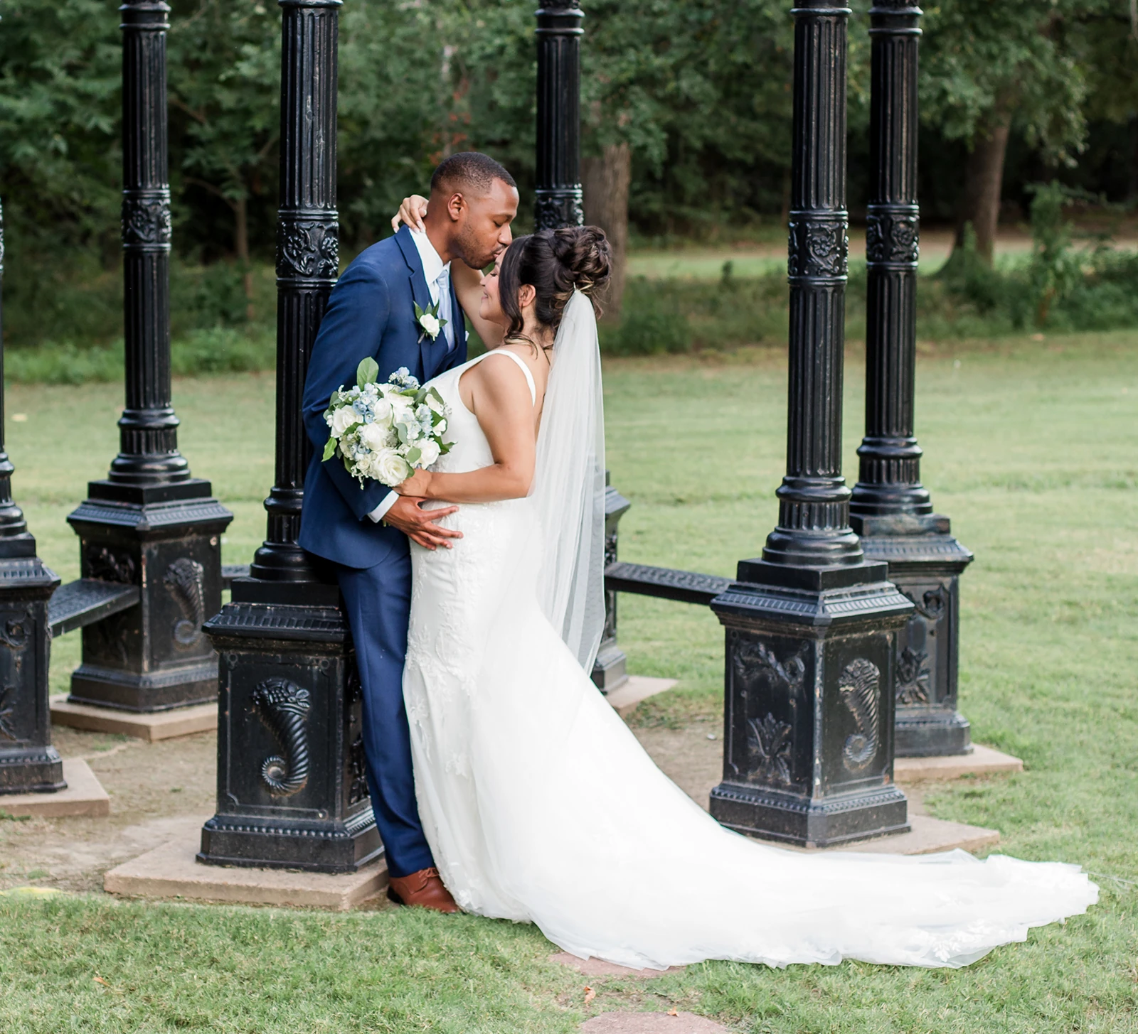 Bride and groom sharing a kiss beside a black decorative gazebo structure during their outdoor wedding portraits