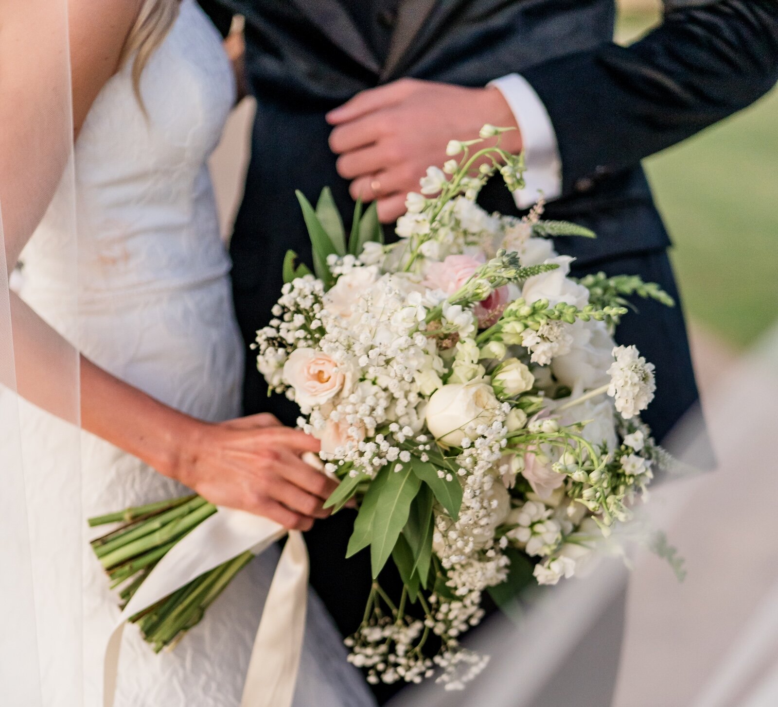 Torso of bride holding wedding bouquet next to groom