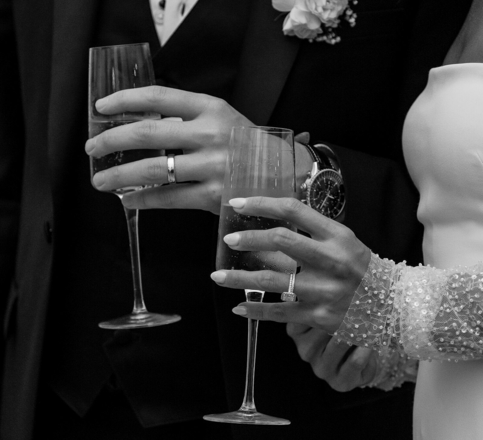 Black and white closeup of bride and groom's newly ringed hands holding champagne flutes