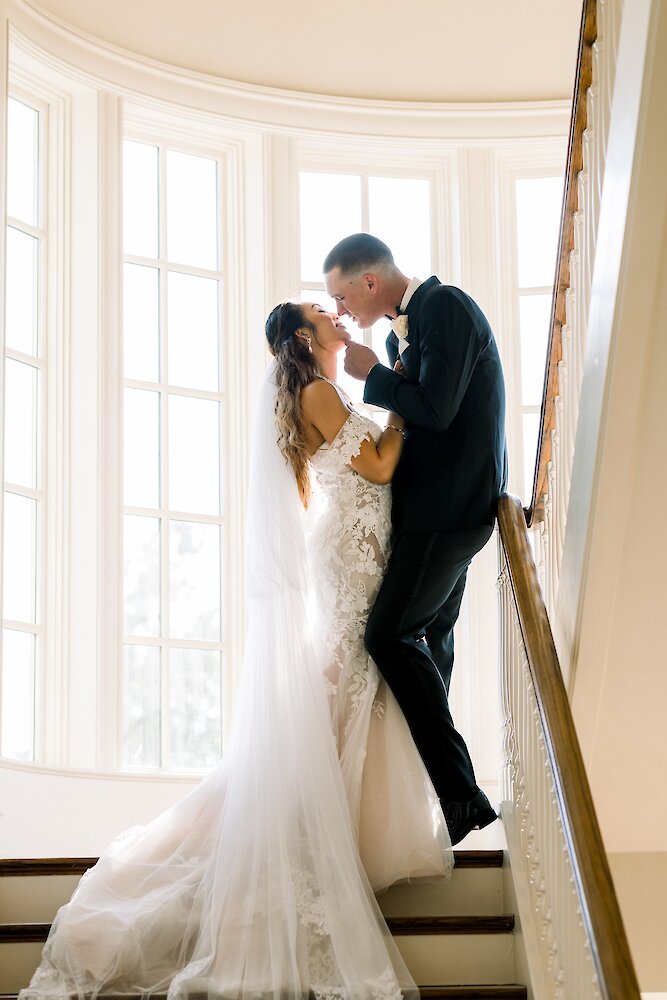 Bride and groom kiss on a sun-drenched stairwell