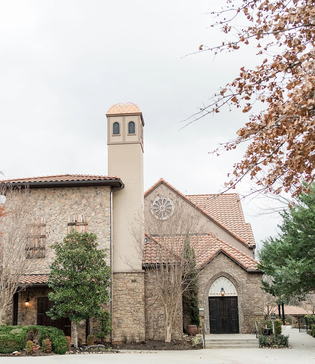 Mediterranean-style stone wedding venue with terracotta roof surrounded by autumn trees and greenery