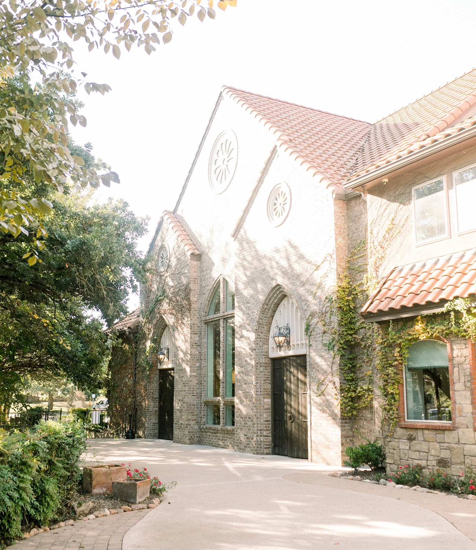 Sunlit Mediterranean-style stone wedding venue with arched windows, terracotta roof tiles, and ivy-covered walls.
