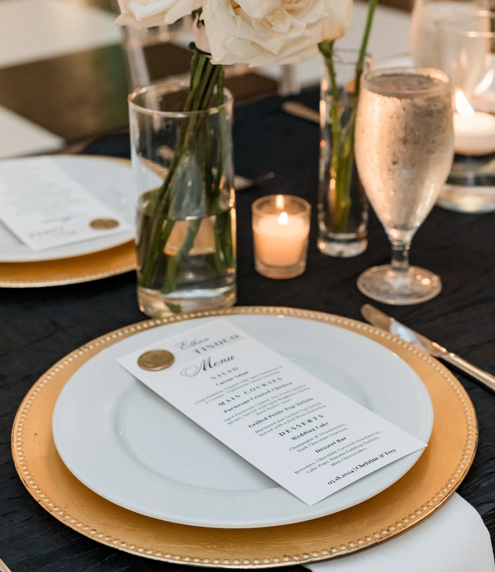 Elegant wedding reception setup with black tablecloths, clear acrylic chairs, and tall white floral centerpieces in a bright ballroom